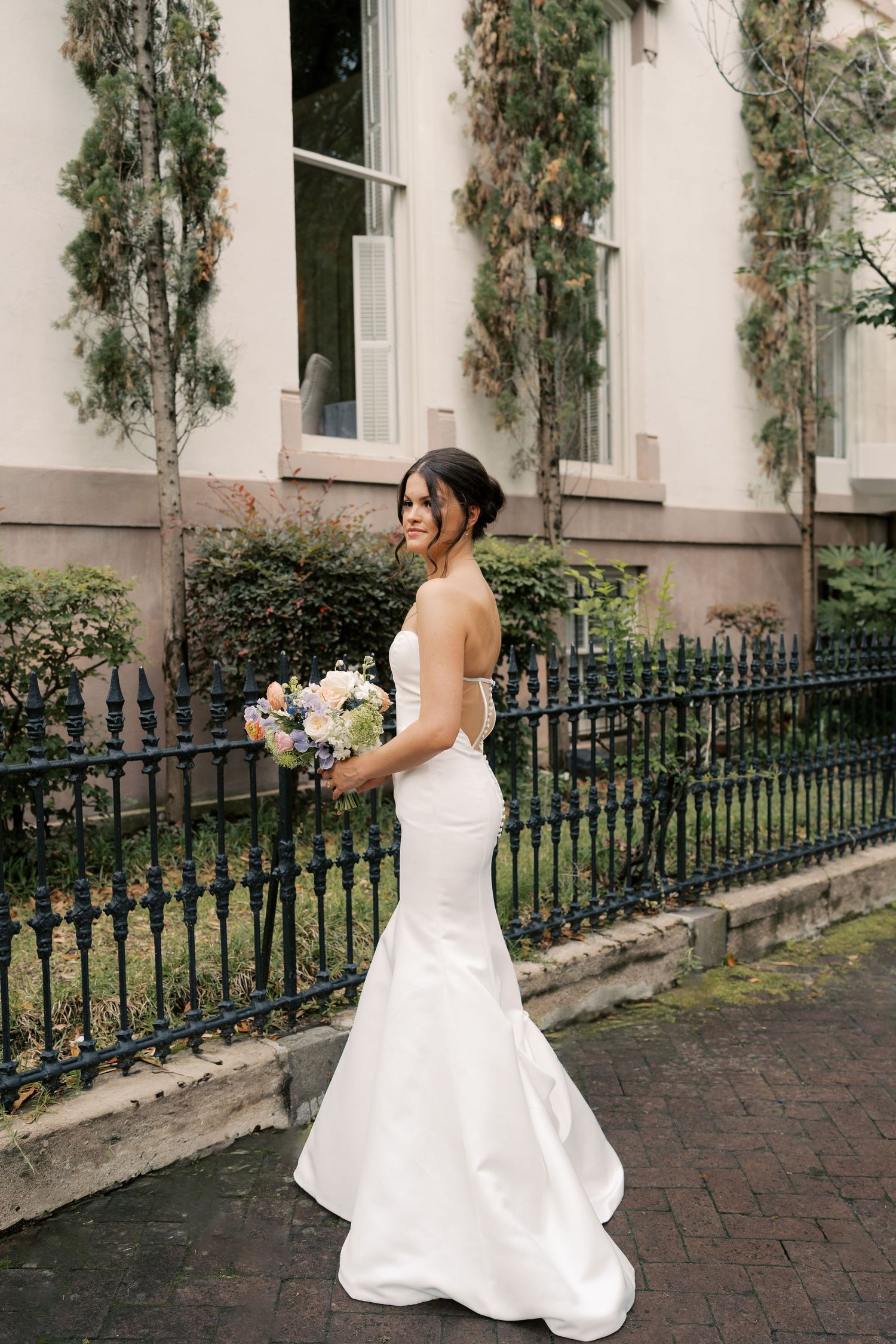 Elegant white mermaid wedding dress photographed against a historic building with climbing vines.