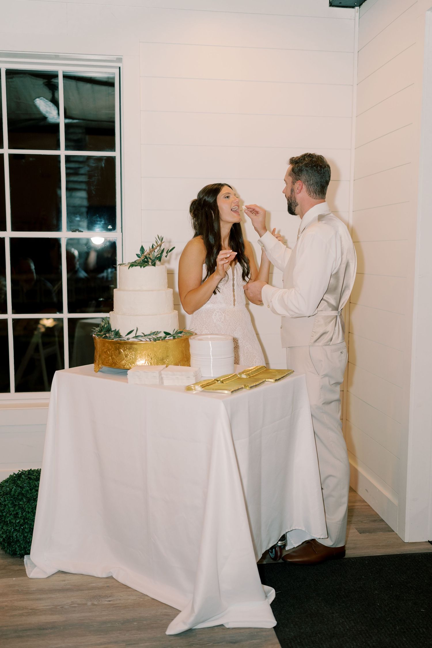 Couple enjoying cake cutting moment at wedding reception in white modern venue.
