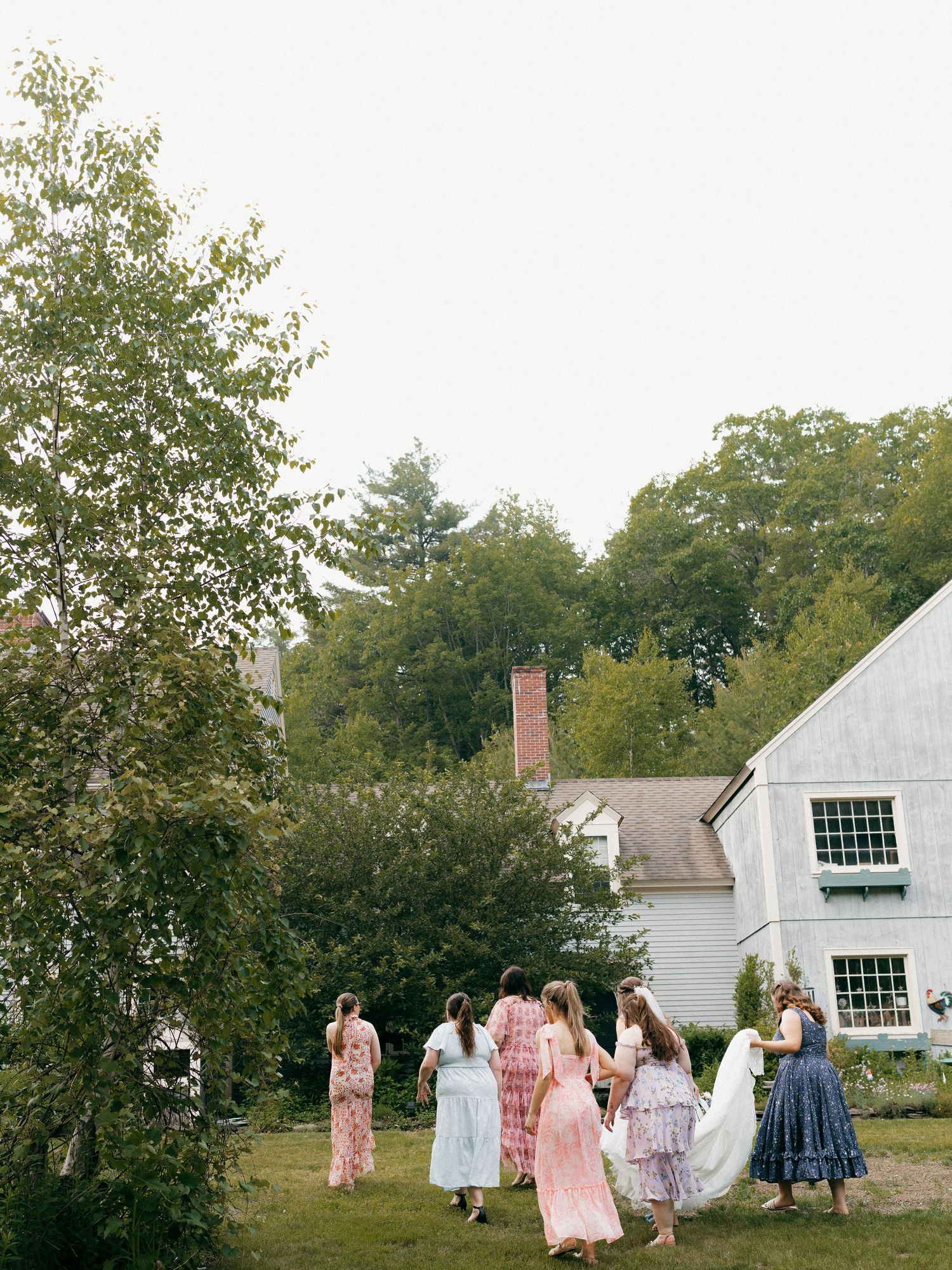 Wedding celebration outside a white colonial-style house with guests in pastel dresses.