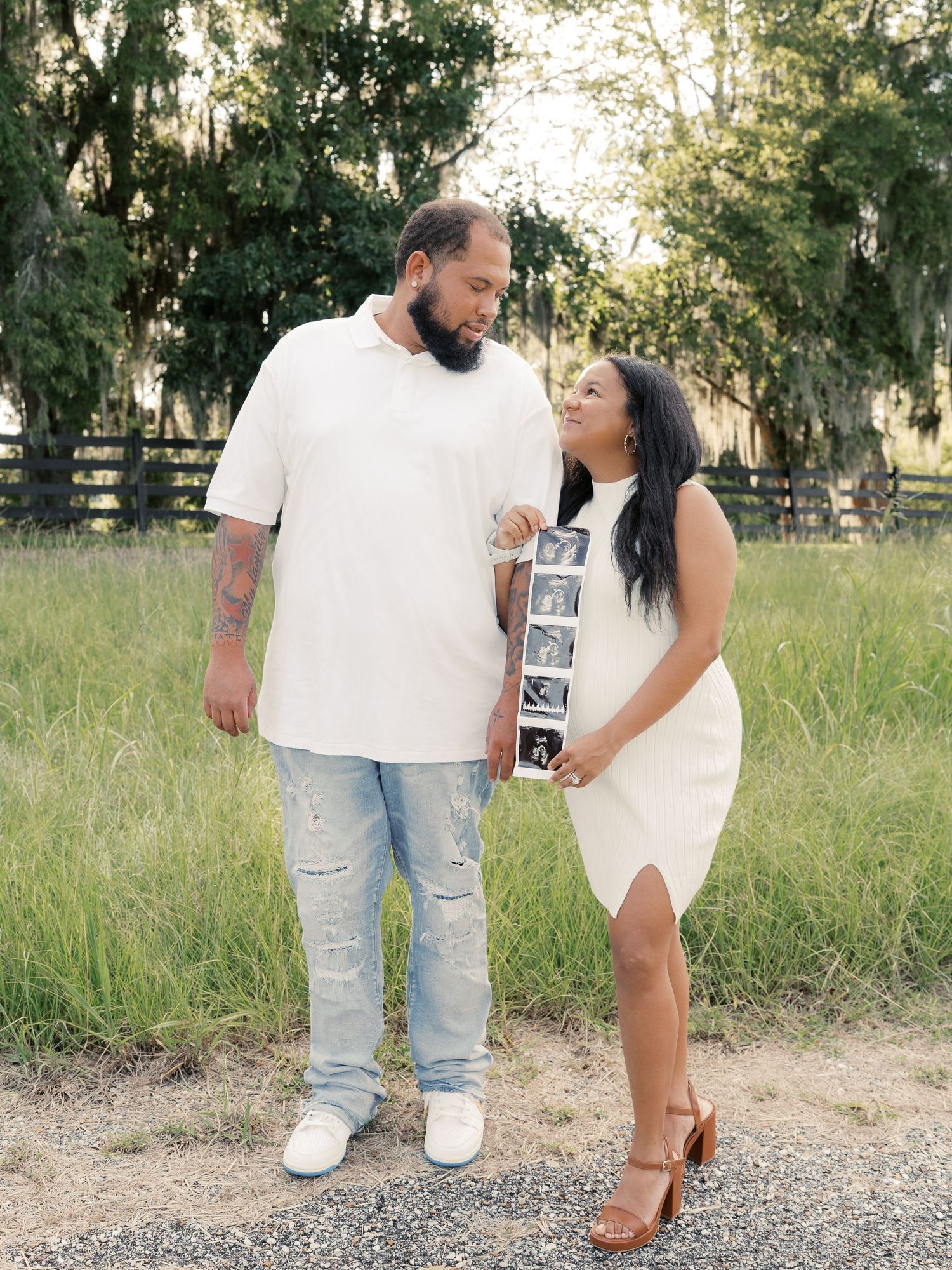 A family poses outdoors holding ultrasound photos in a grassy field during sunset.