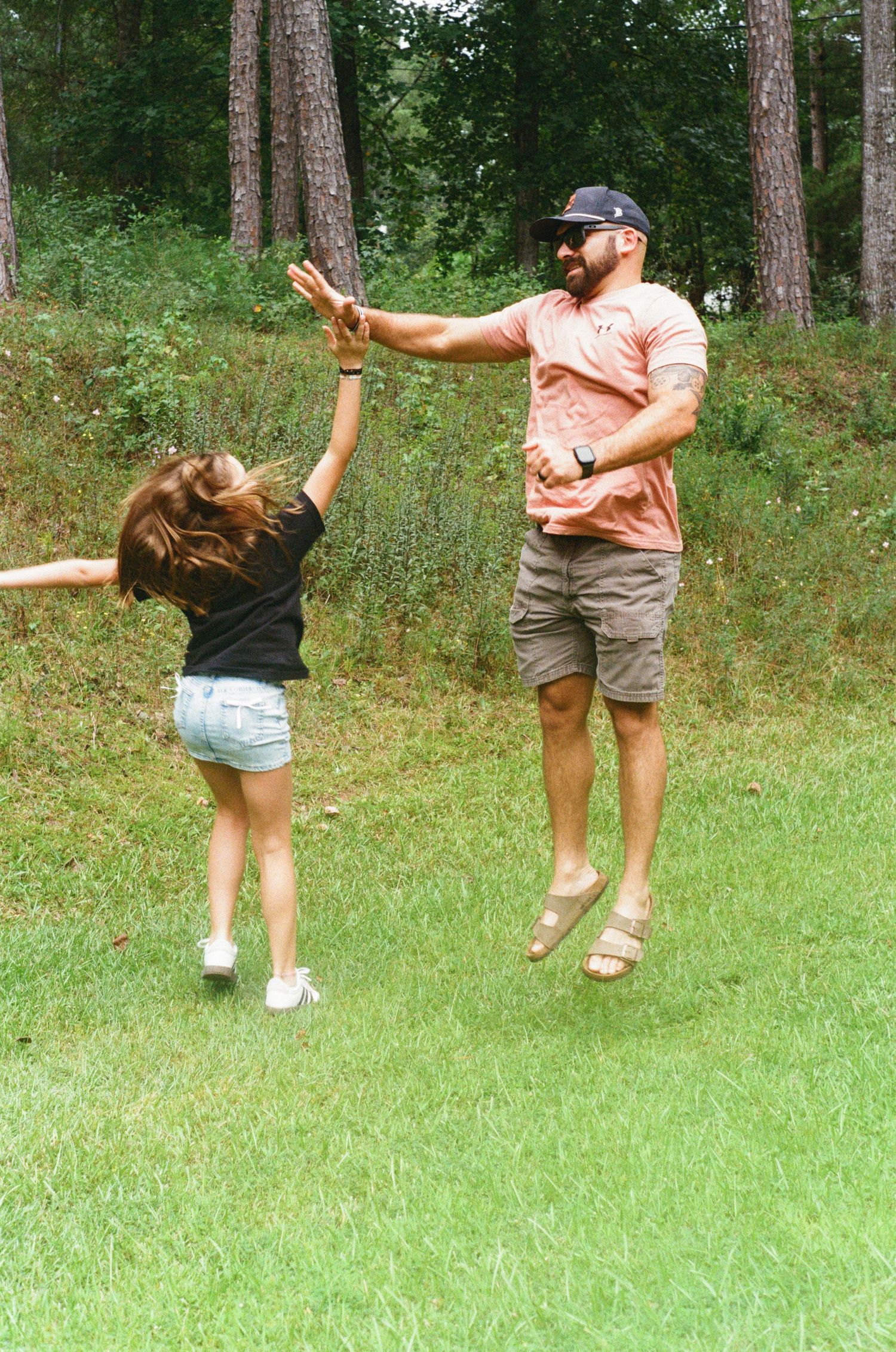 Dynamic sequence of people leaping and playing on grass in a wooded outdoor setting.