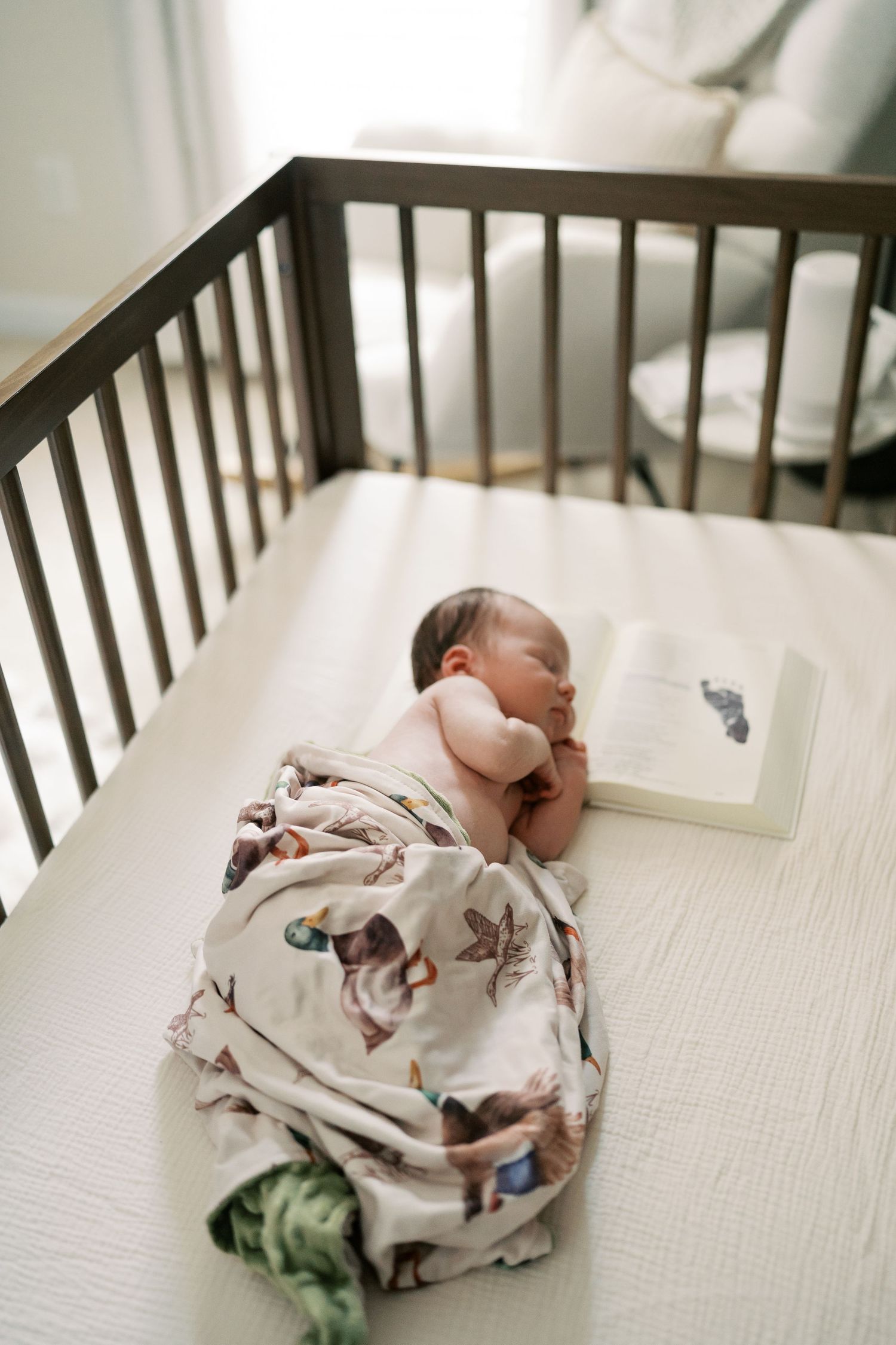 Newborn baby sleeping peacefully in wooden crib with white bedding.