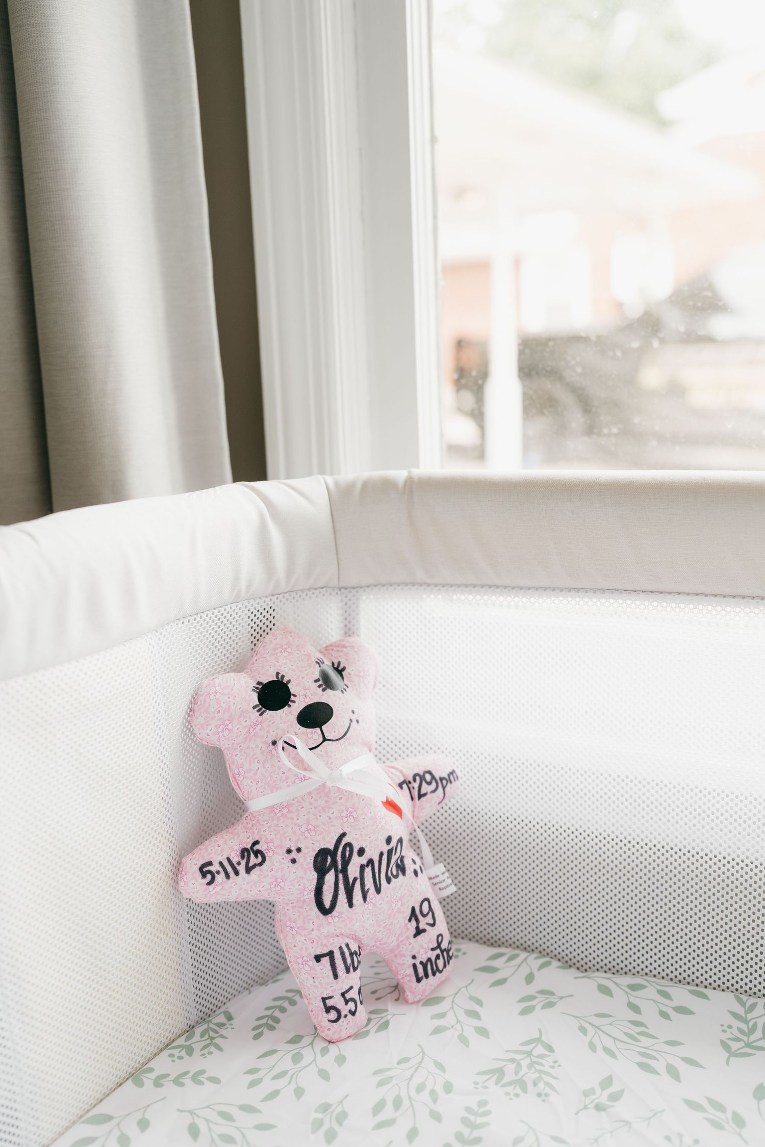 Pink teddy bear decorations displayed in white baby crib near window.