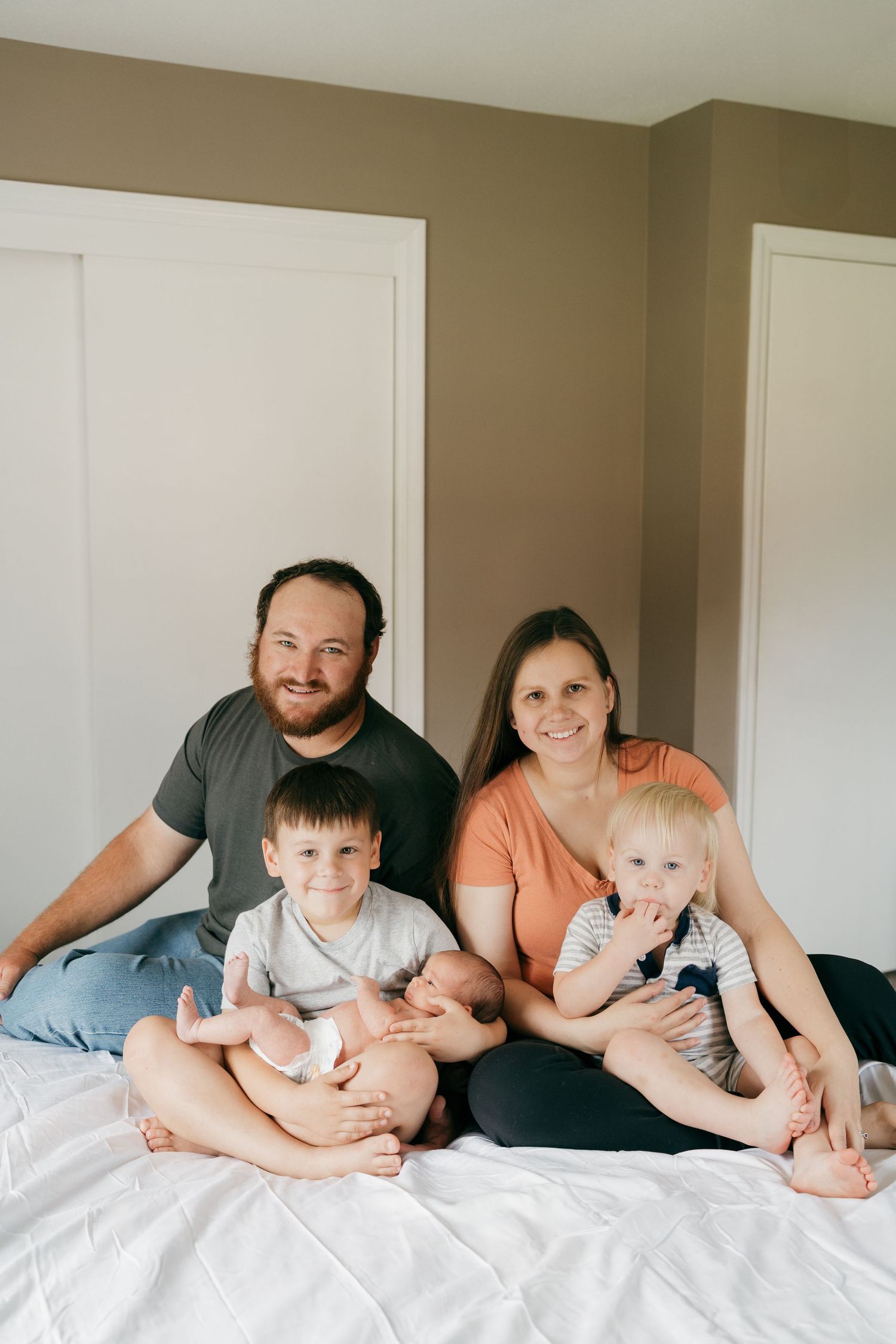 Family lounging together on white bedding during an intimate lifestyle photography session.