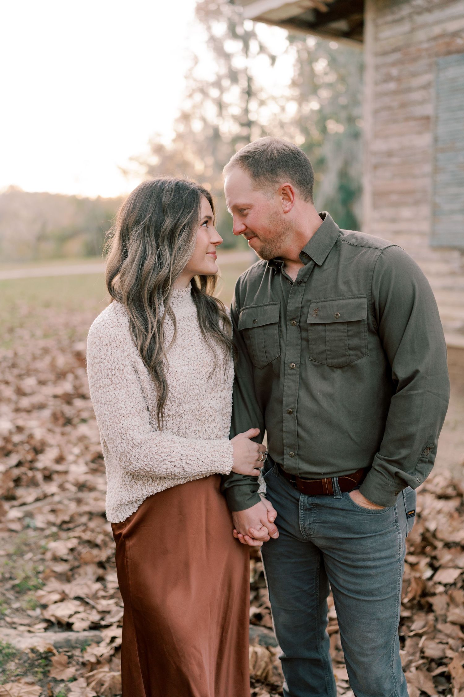 A couple shares an intimate moment while standing in autumn leaves outside a brick building.