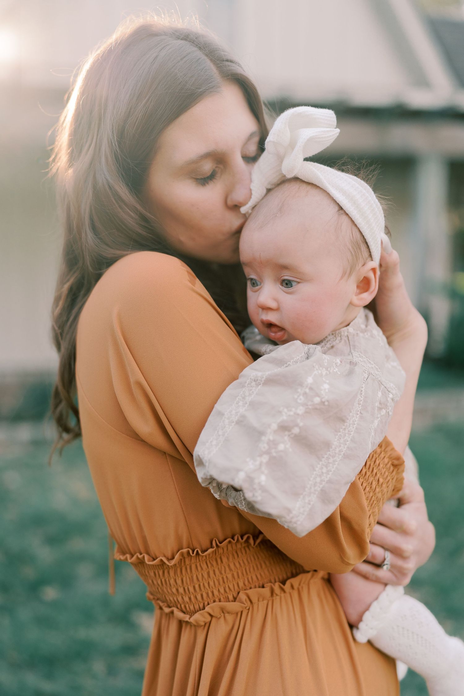 A parent in a rust-colored dress cradles and embraces a baby wearing white lace.