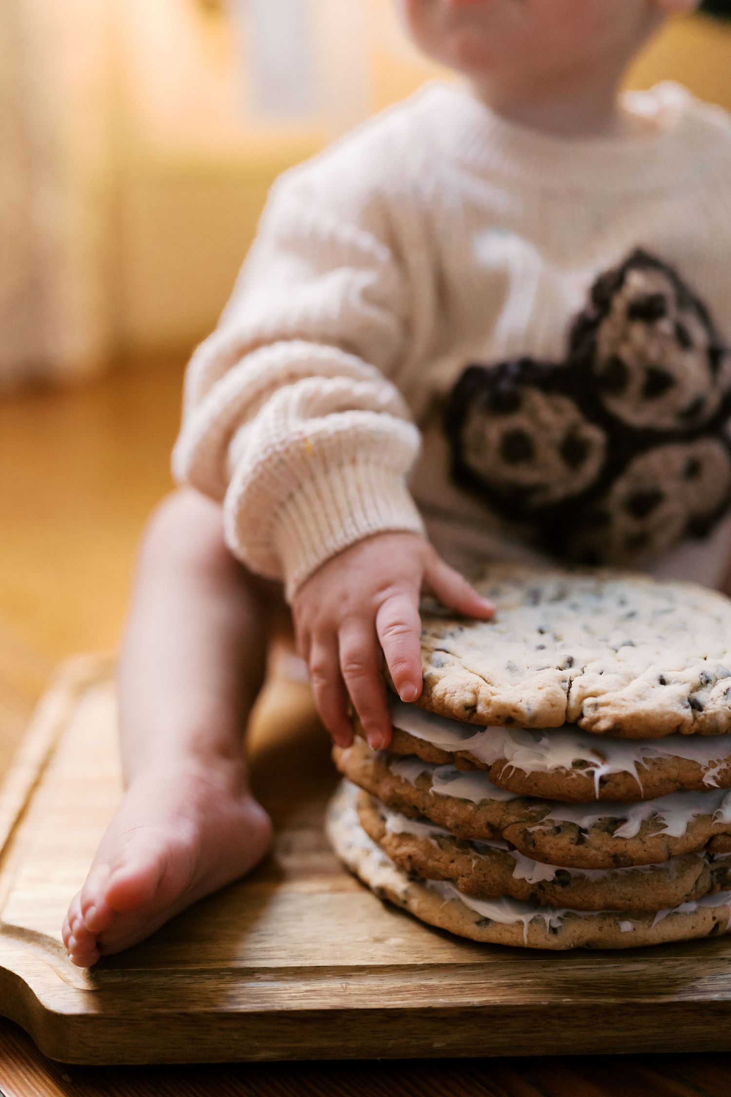 Close-up of baby's hands reaching for stacked cookies on wooden surface.