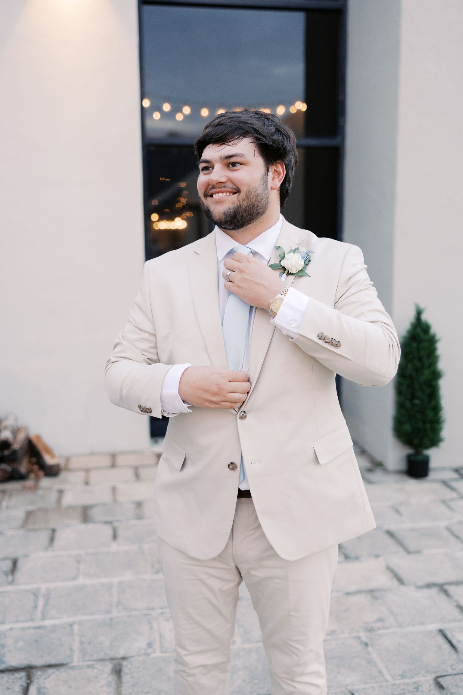 A groom in a cream colored suit smiles and laughs during wedding day portraits on stone steps.