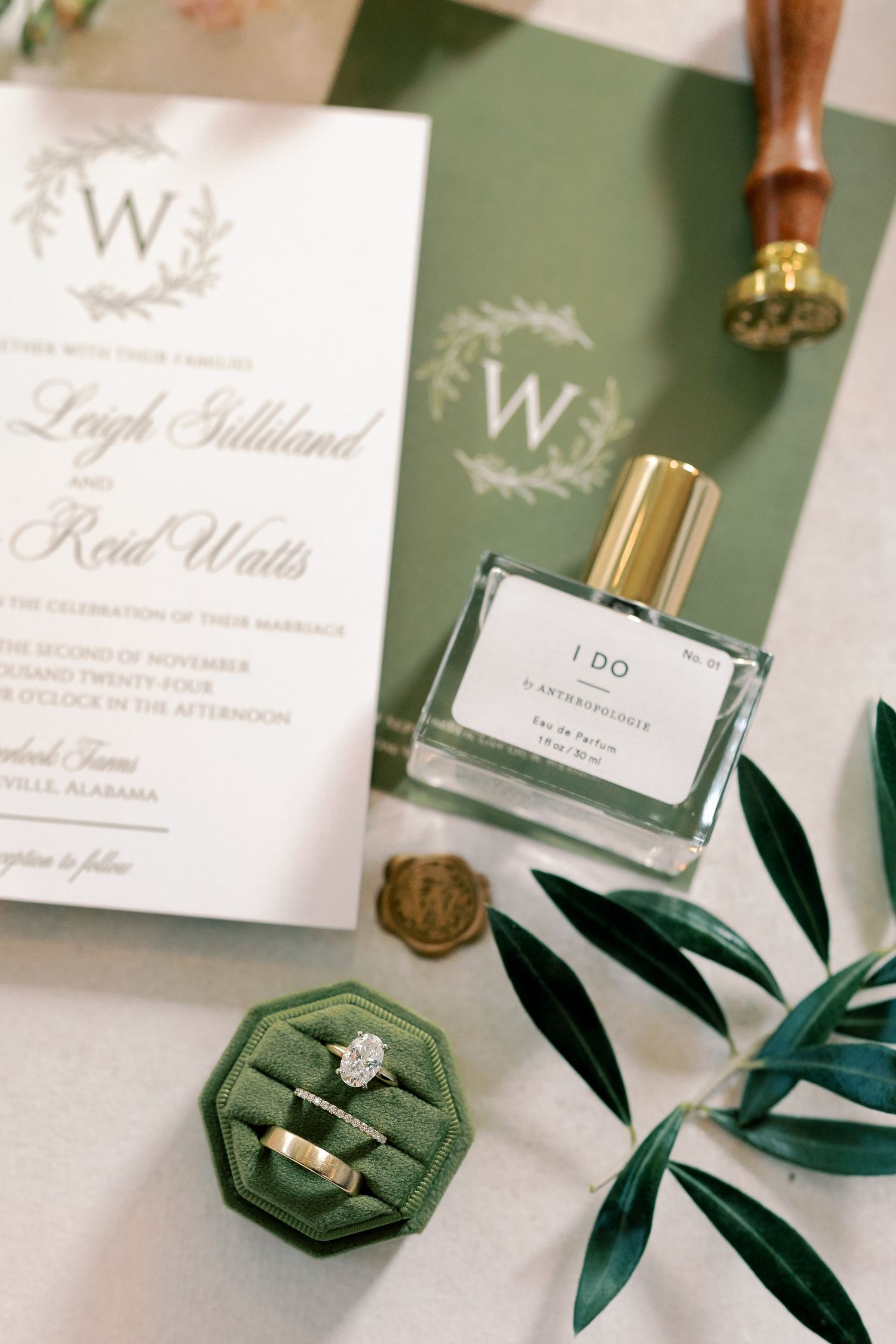 Wedding invitation suite with green velvet ring box and olive leaves on display.