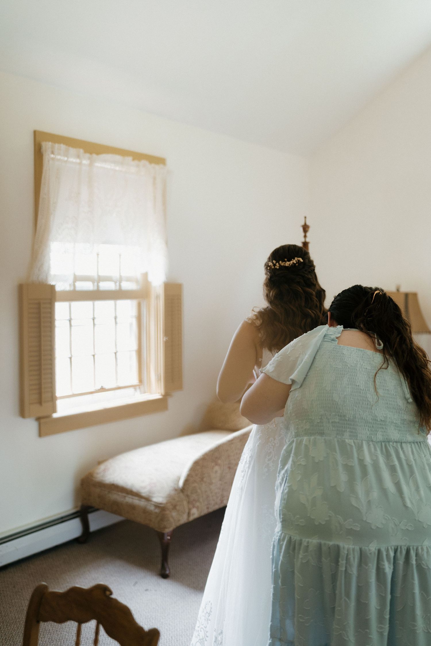 A light mint green dress and white veil shown in a sunlit bedroom.