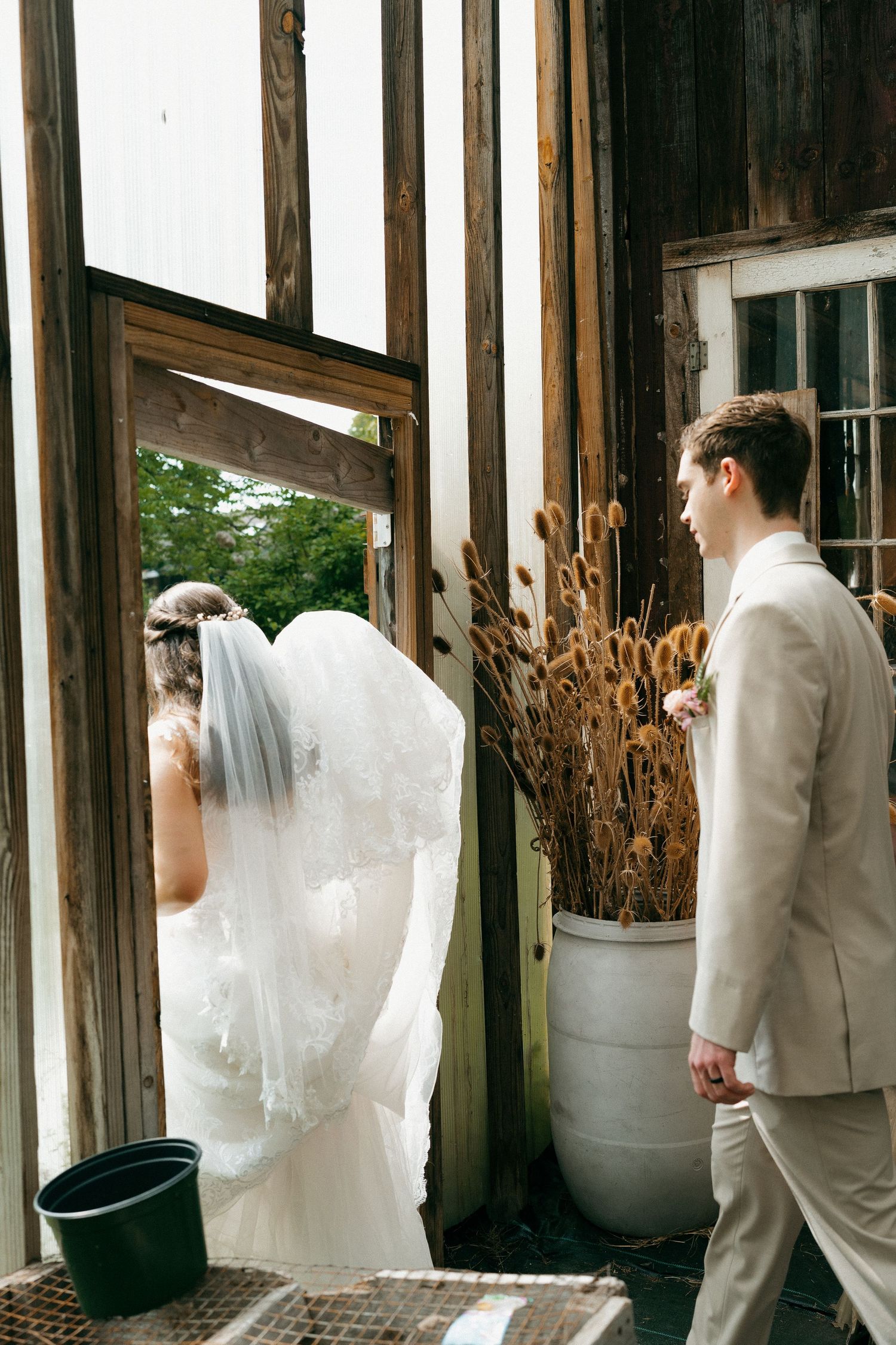 Wedding party in white and cream attire posing against rustic wooden wall.