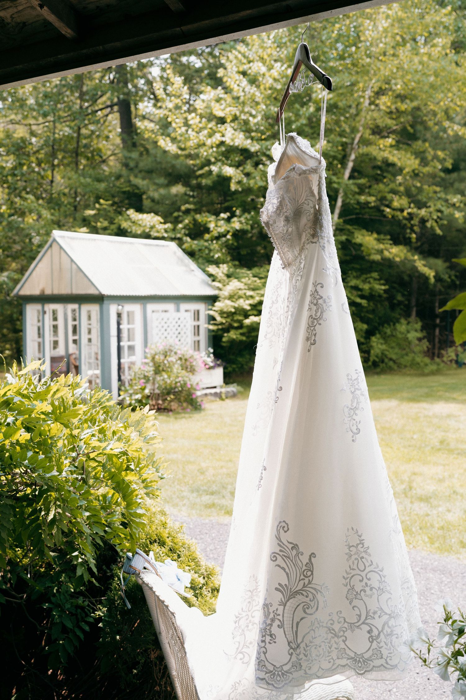 Elegant white wedding gown with embroidered details displayed outdoors against lush greenery.