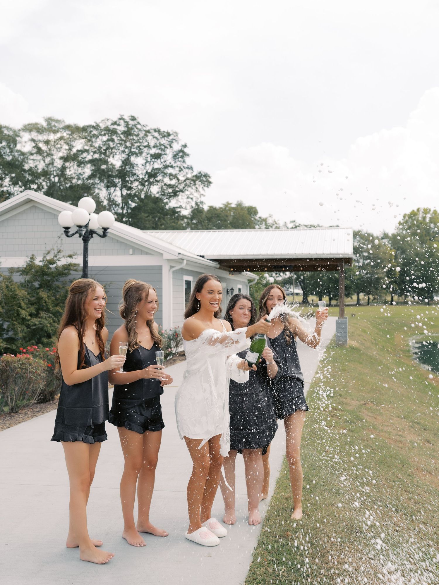 Wedding party in black robes relaxing on porch swing with decorative teal garlands.
