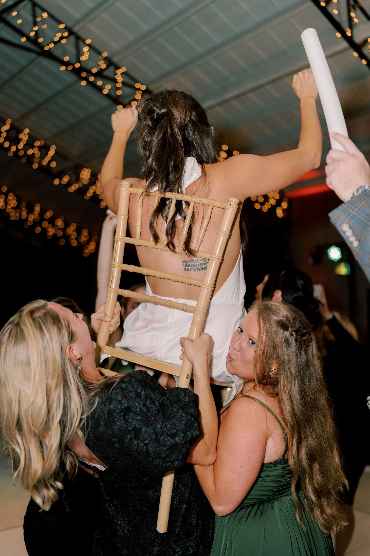 Wedding guests lifting someone in chair during traditional celebration dance.