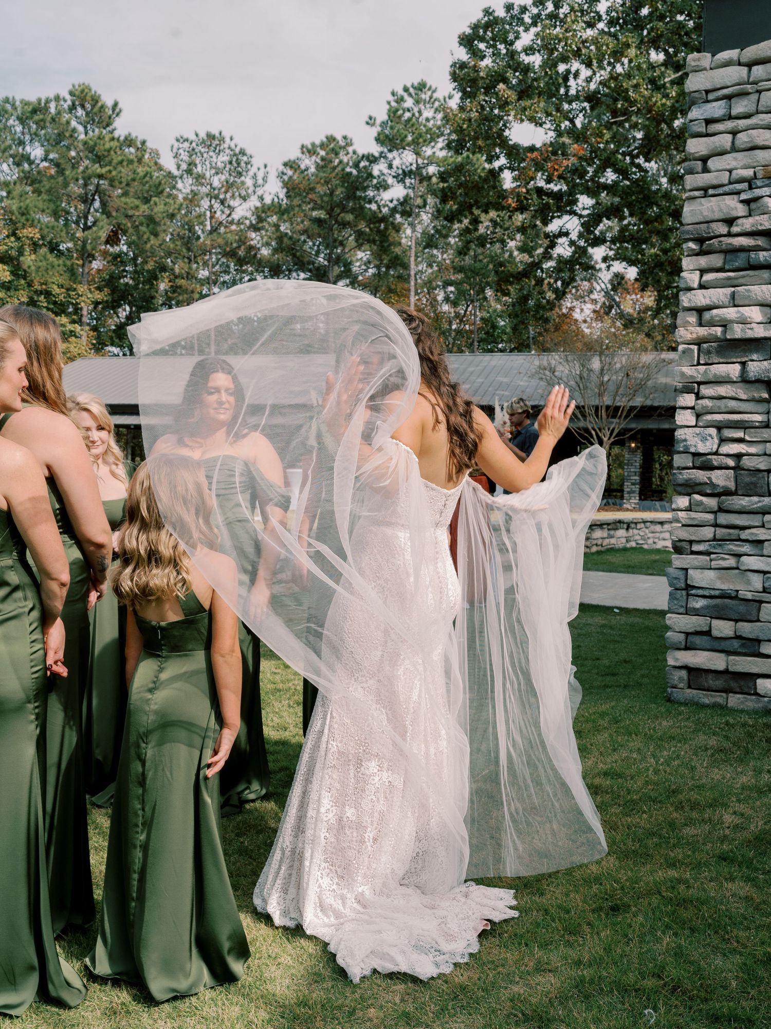 Wedding party celebrates outdoors with flowing dresses and veils catching the breeze.