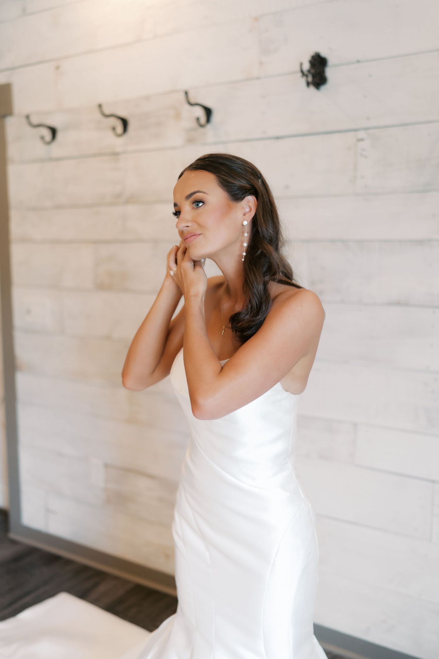 Person in white dress preparing for special occasion against rustic white wall.