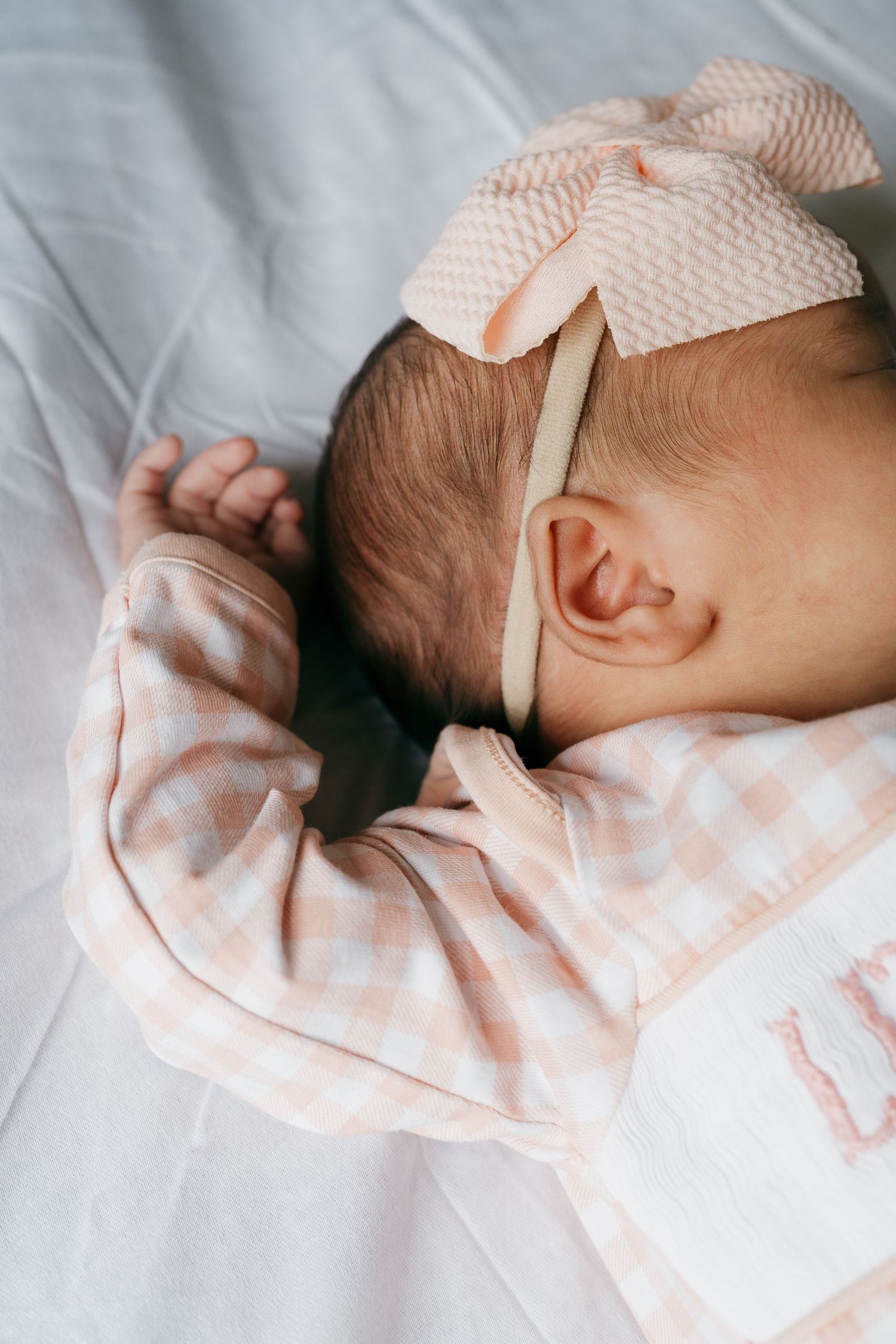 Close-up details of sleeping newborn wearing pink gingham outfit.