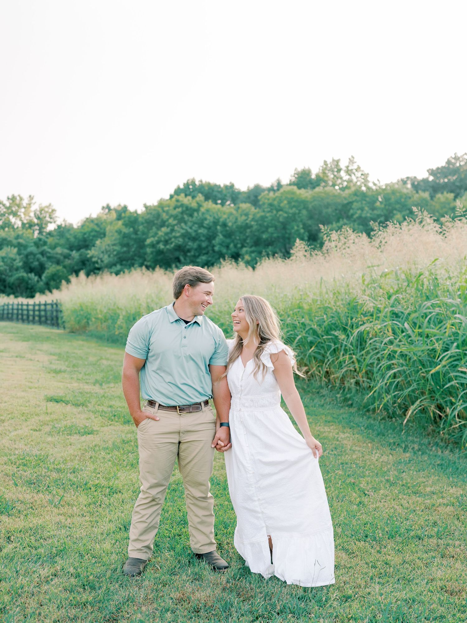 Couple in coordinating white and blue outfits walking together through grassy field.