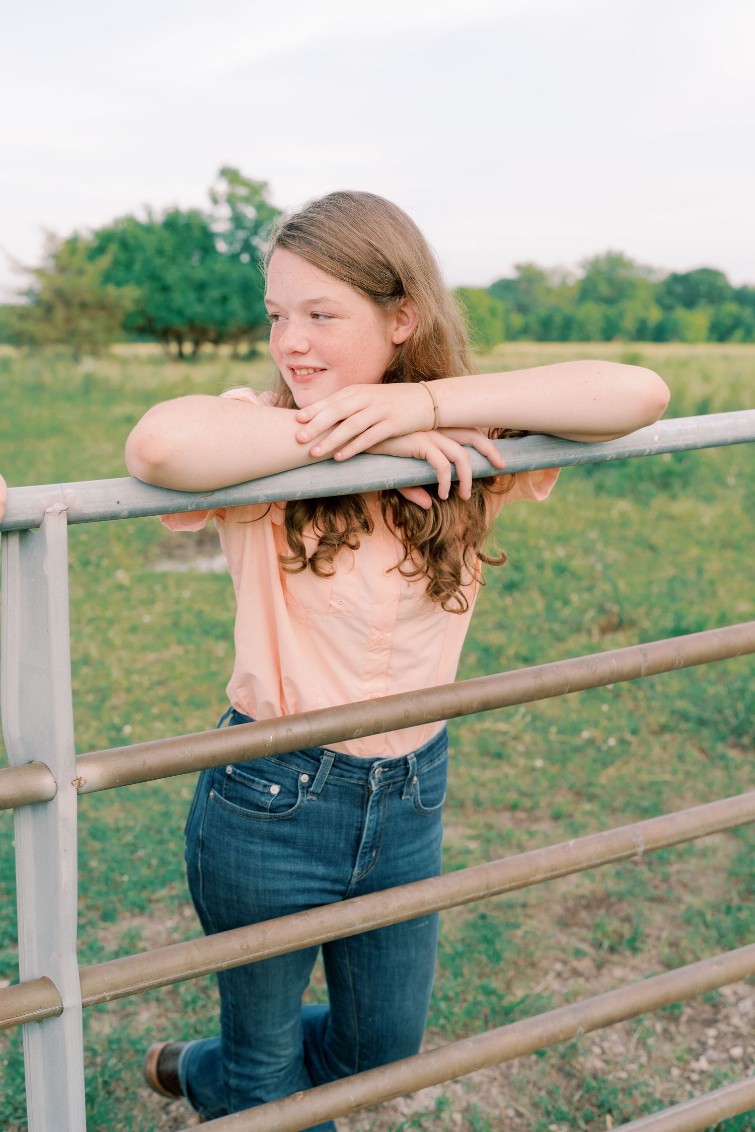 Person in peach shirt leans on metal fence rail while smiling.