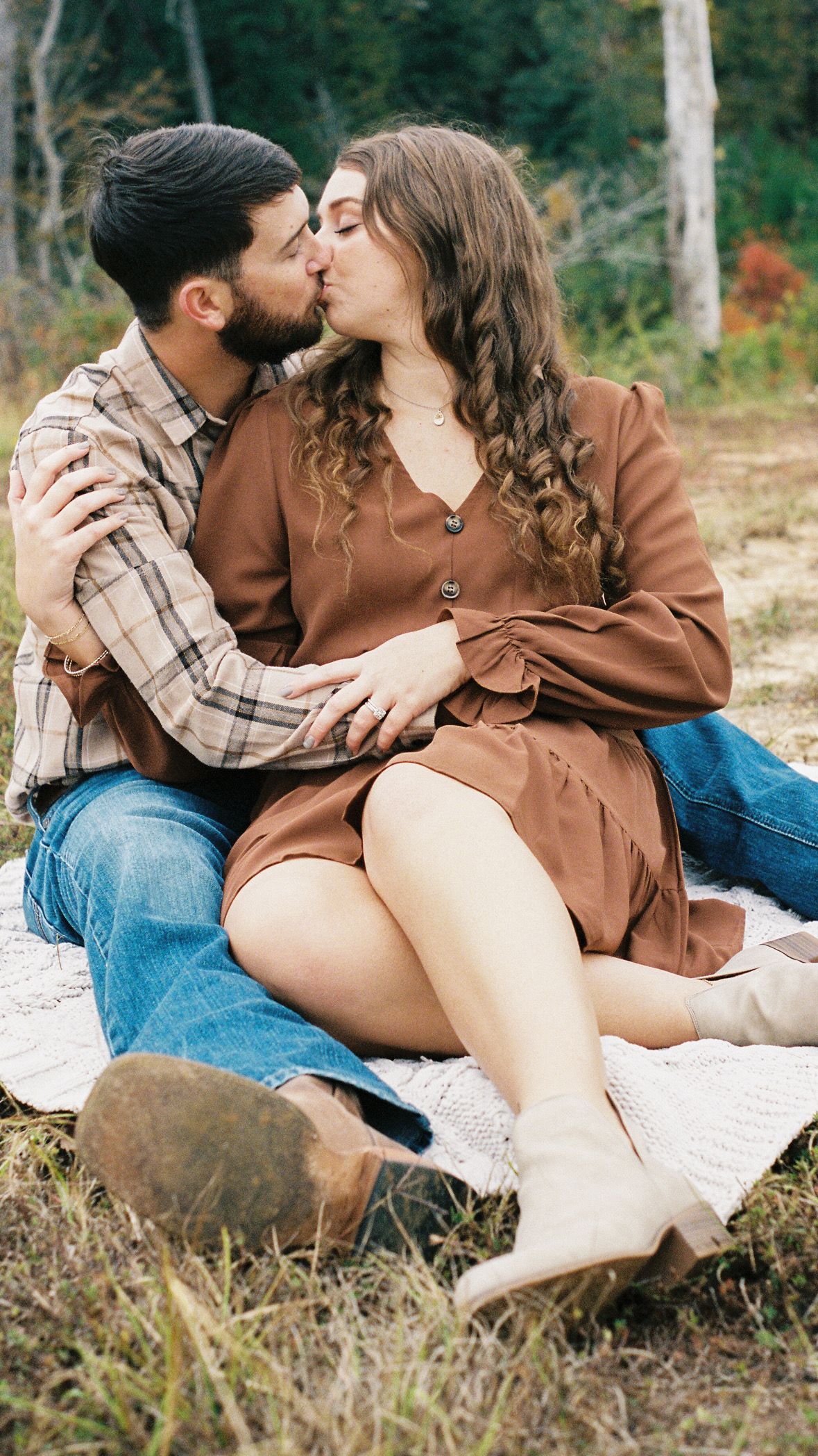 Couple in casual fall attire sharing an intimate moment on a blanket outdoors.