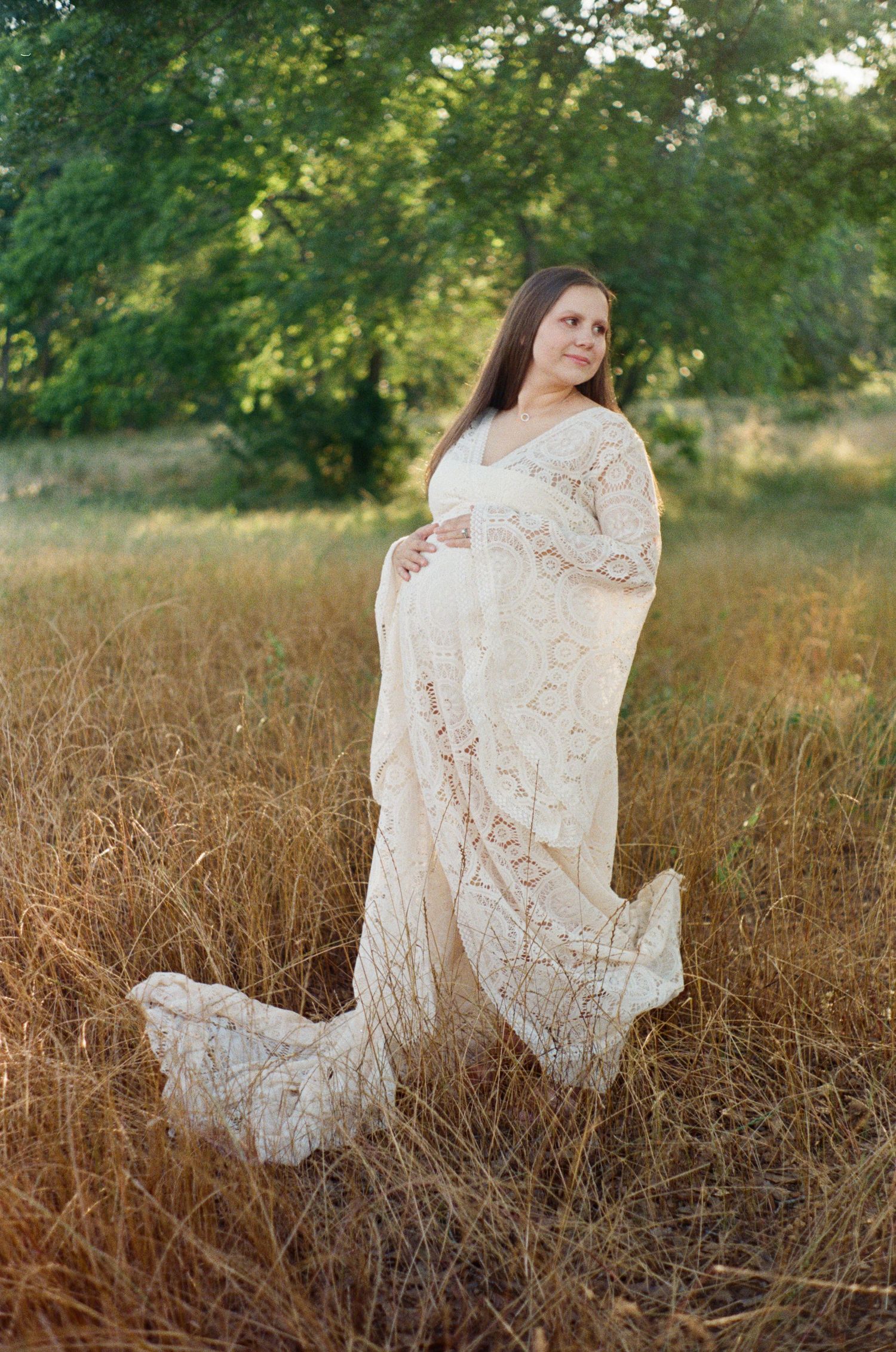 Person in white lace dress posing in a golden field during sunset.