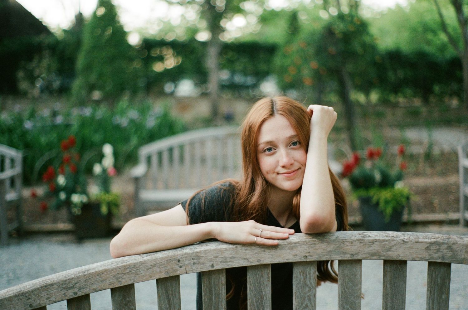 Person relaxing on a wooden garden bench with flowers and greenery in the background.
