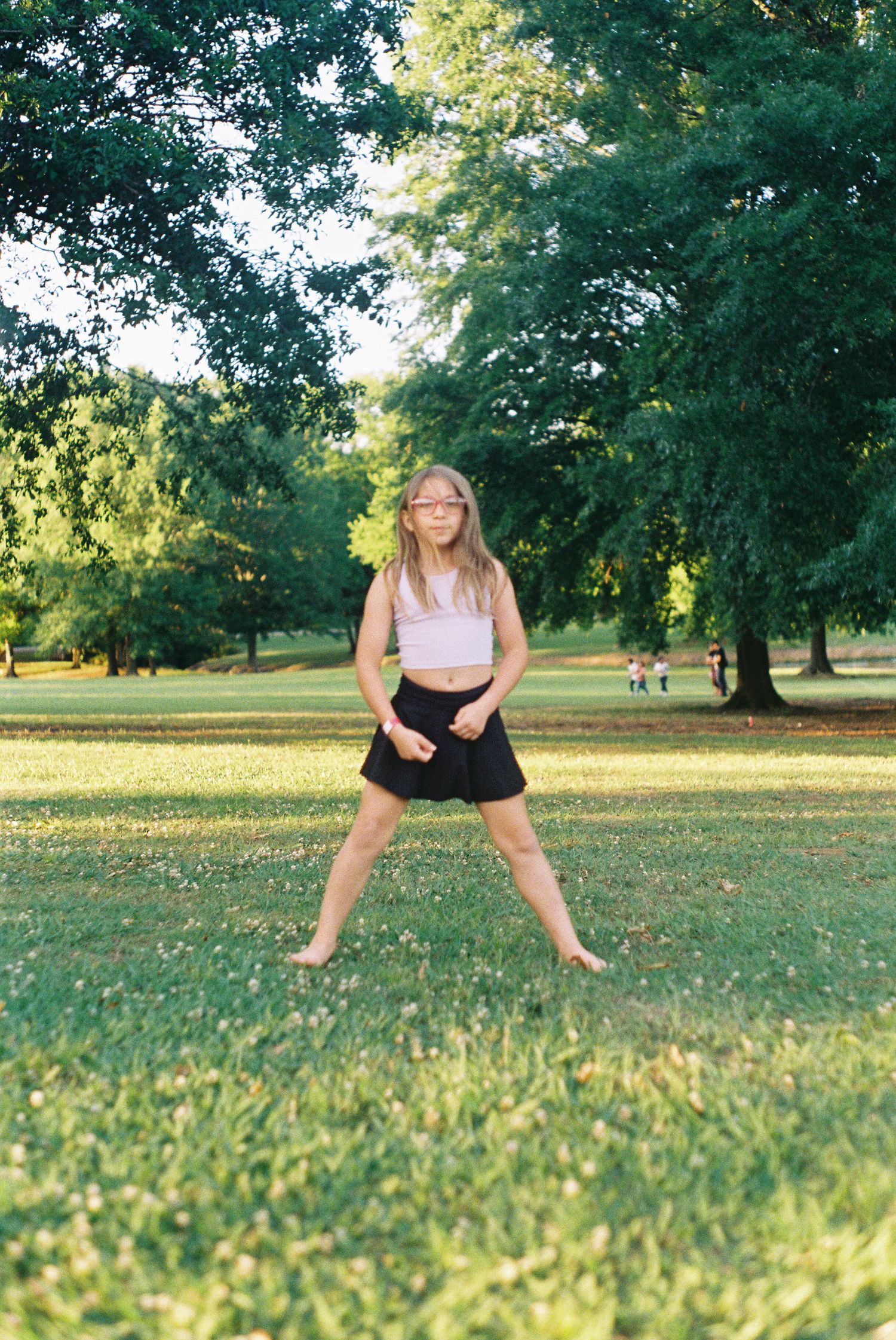 Playful sequence of someone jumping and posing on grass in a sunlit park.