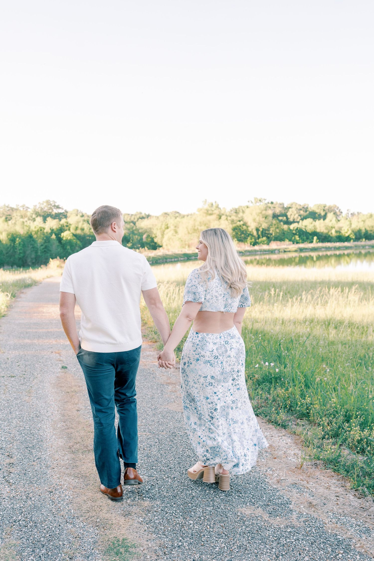 Couple strolls together on gravel path beside marsh at golden hour.