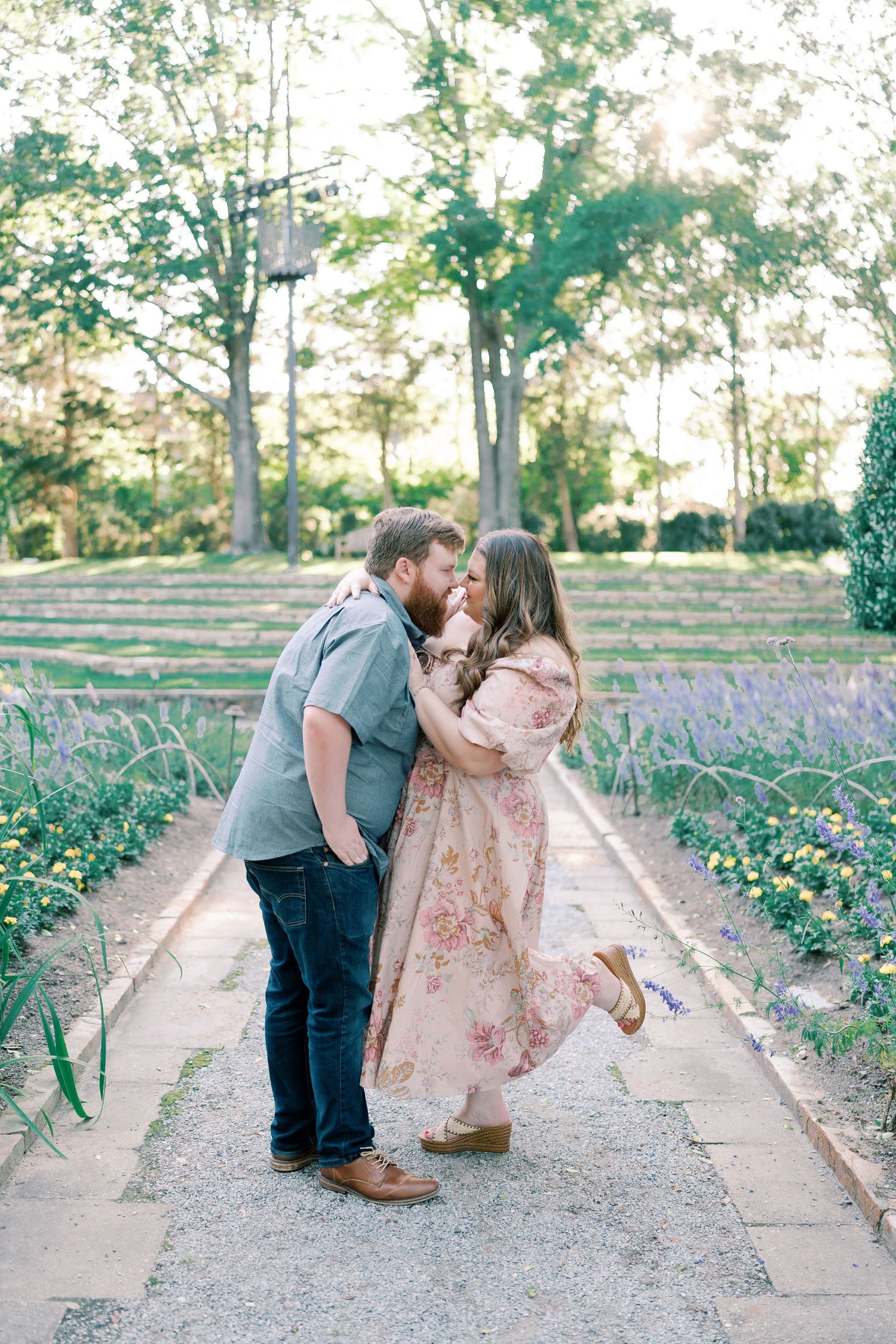 A couple sharing playful moments on a garden path surrounded by blooming flowers.