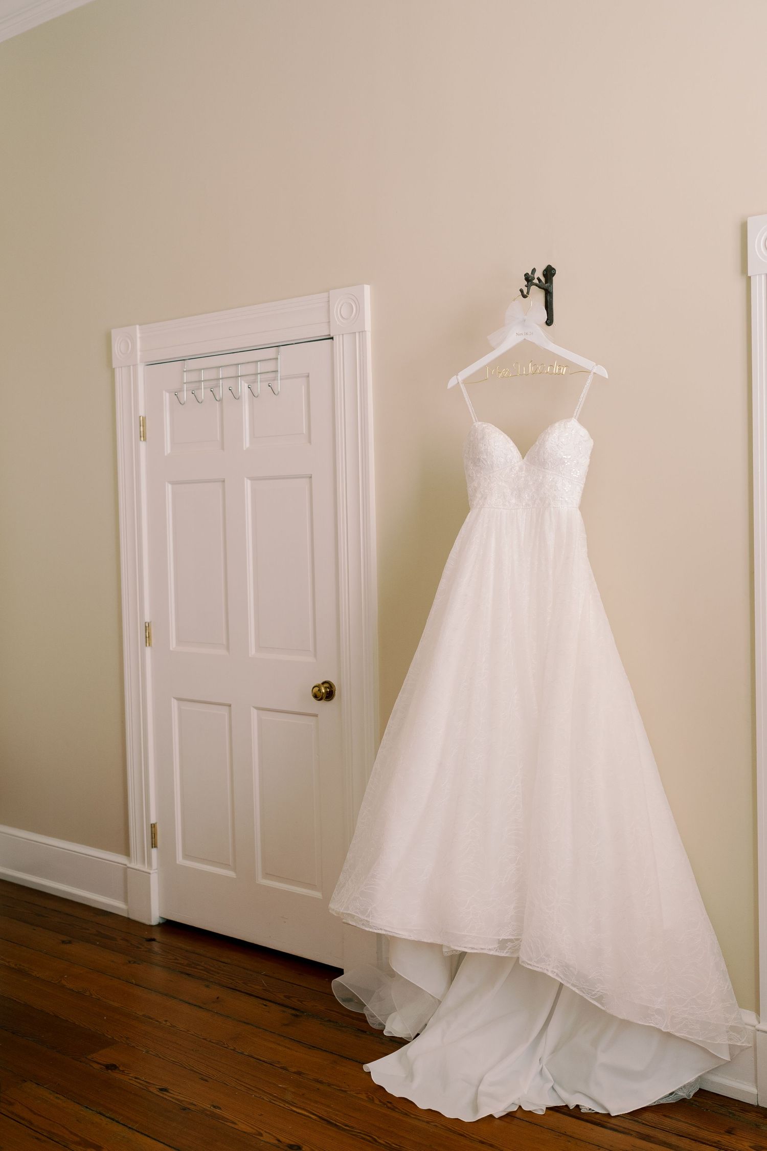 White wedding gown hanging on wall next to wooden door in preparation room.