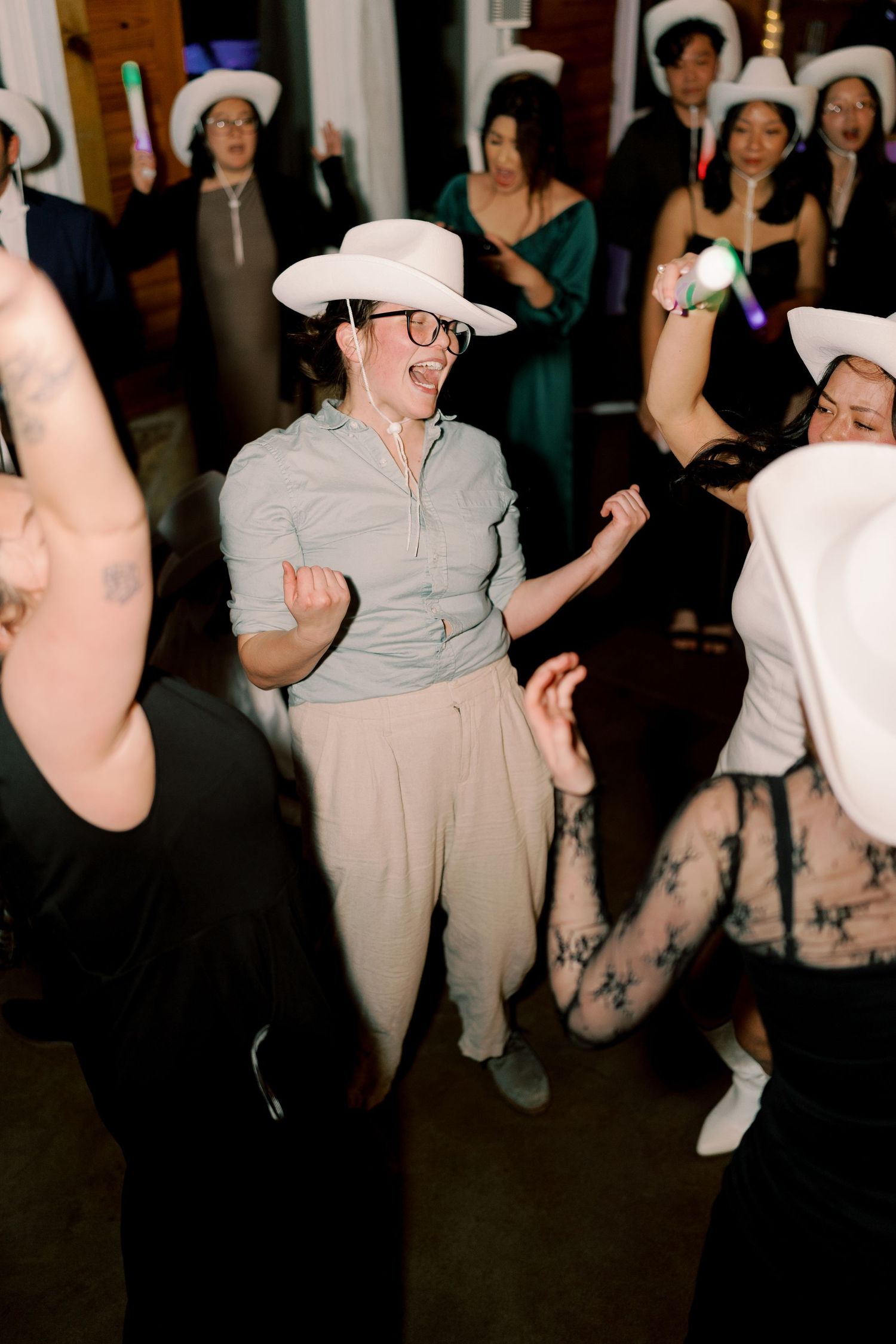 Party guests wearing cowboy hats dancing together in a dimly lit room.