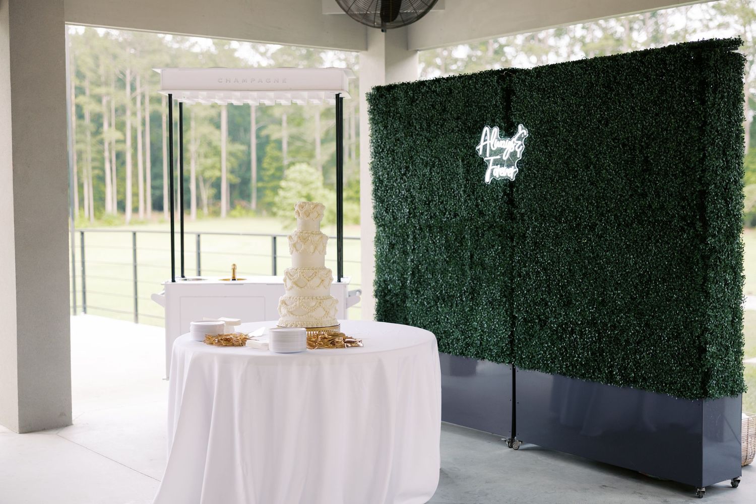 Elegant wedding venue setup with green hedge wall backdrop and white decorative elements.