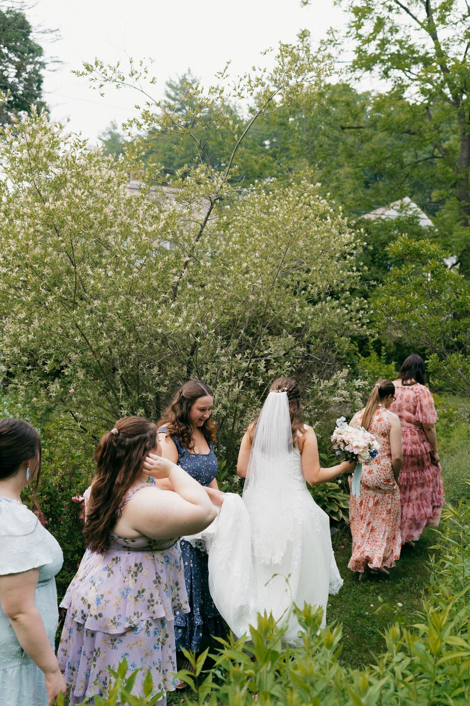 Wedding party helping with the bride's dress in a blooming garden setting.