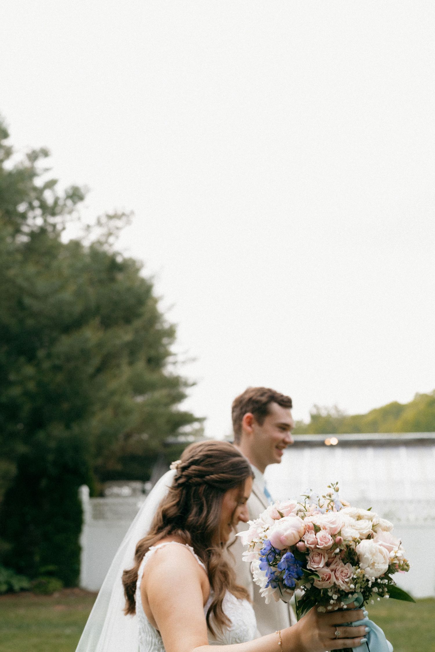 Wedding couple poses by a waterfront with floral bouquets and natural scenery.