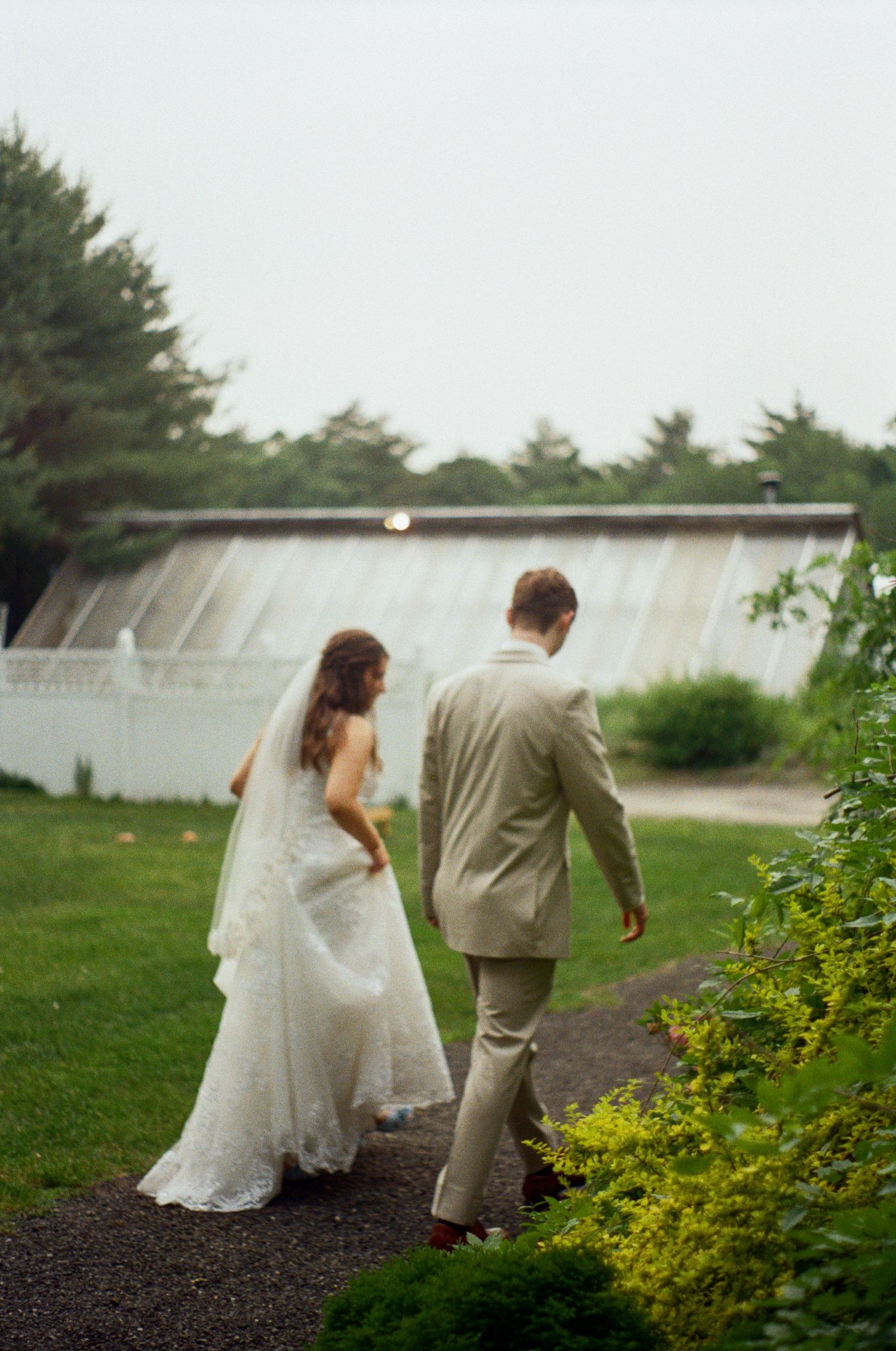 Couple walking through garden path with greenery and white structures.