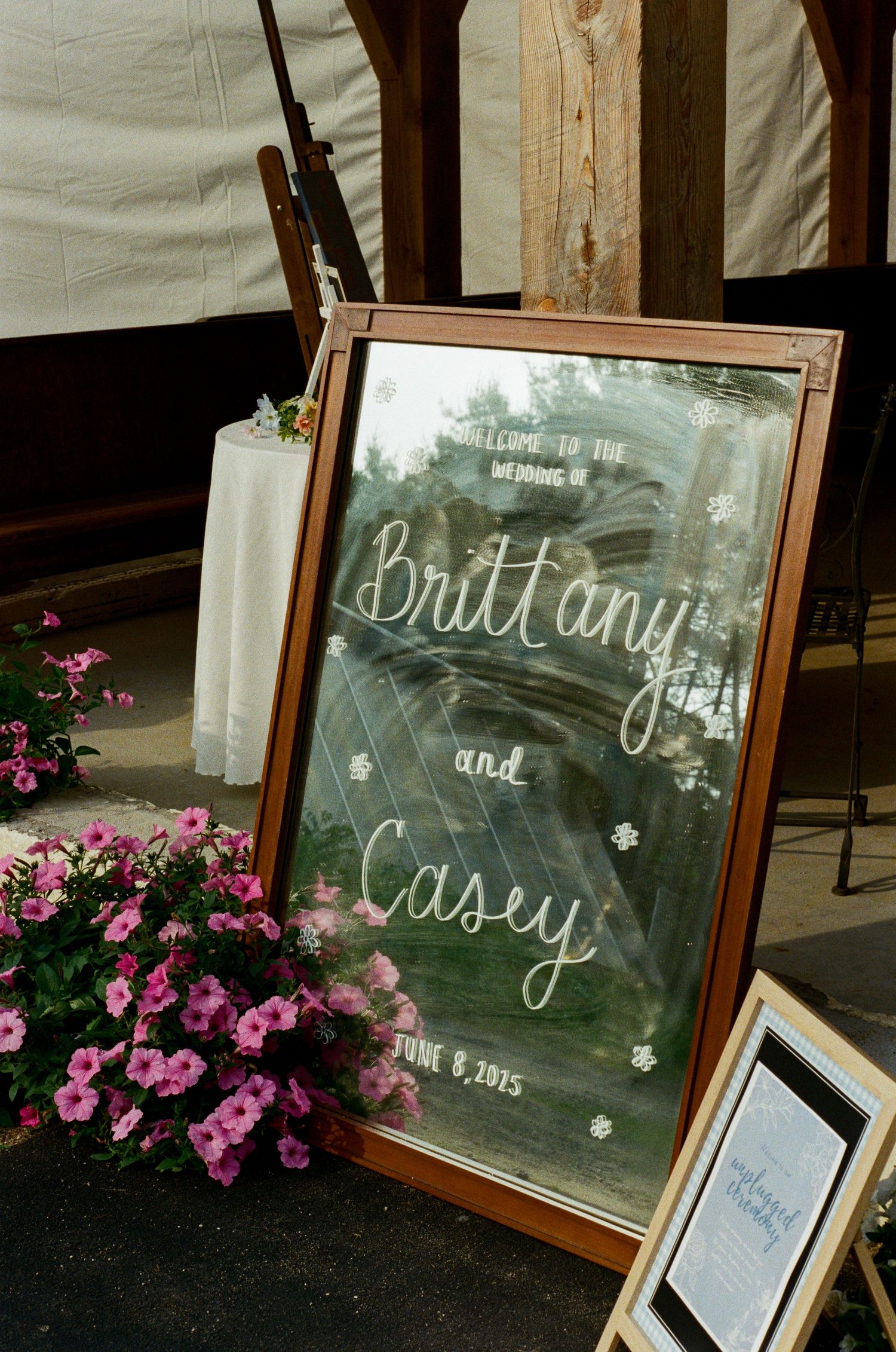 Vintage-style mirrors with handwritten text displayed alongside pink flowers at an event.