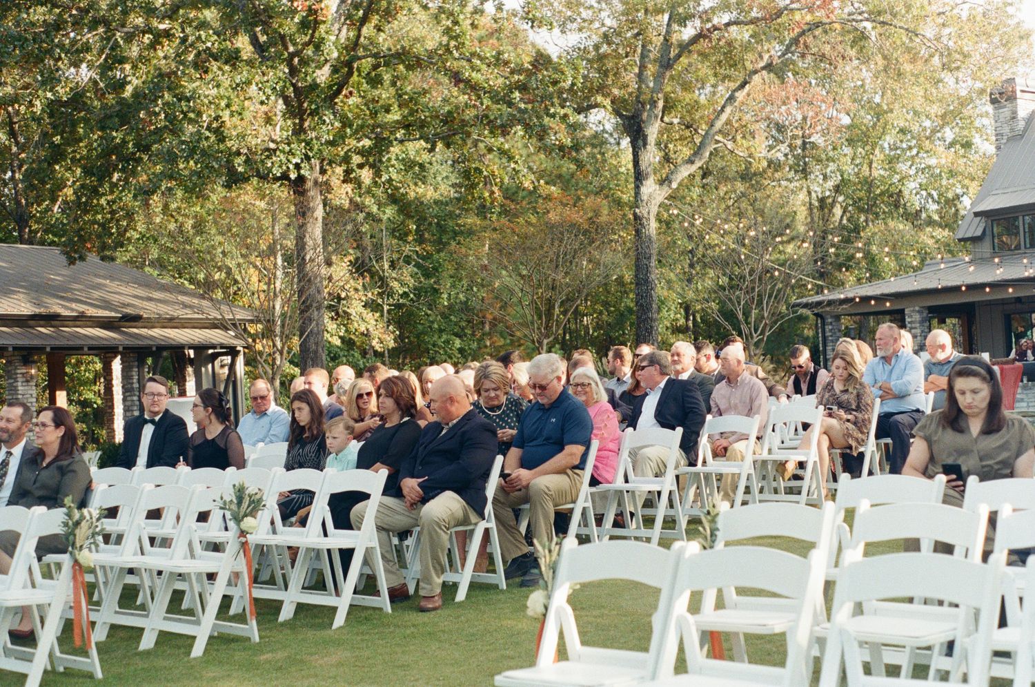 White folding chairs set up in rows for an outdoor wedding ceremony with trees in the background.