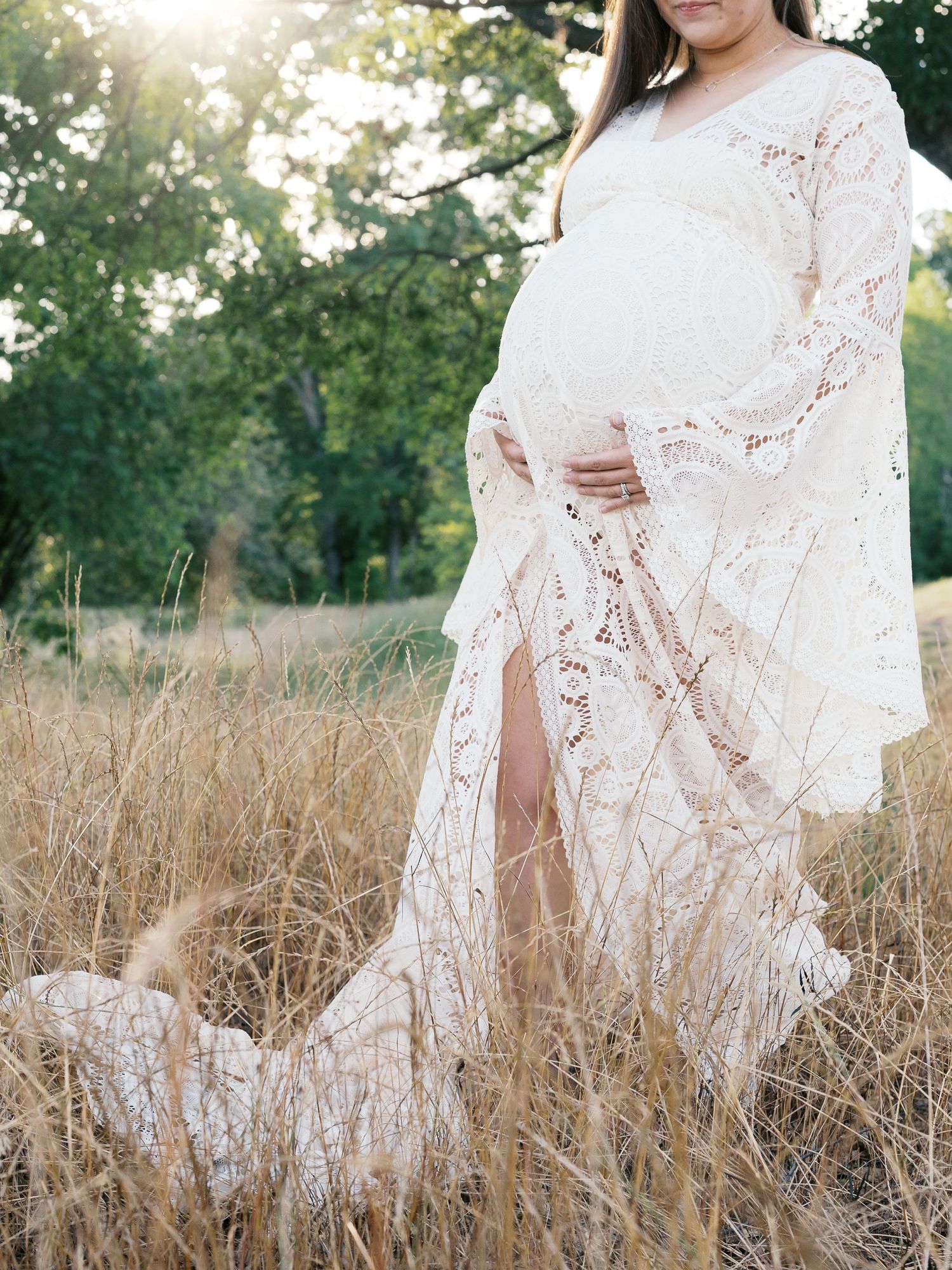Dreamy white lace gown flows through tall grass in golden sunlight.