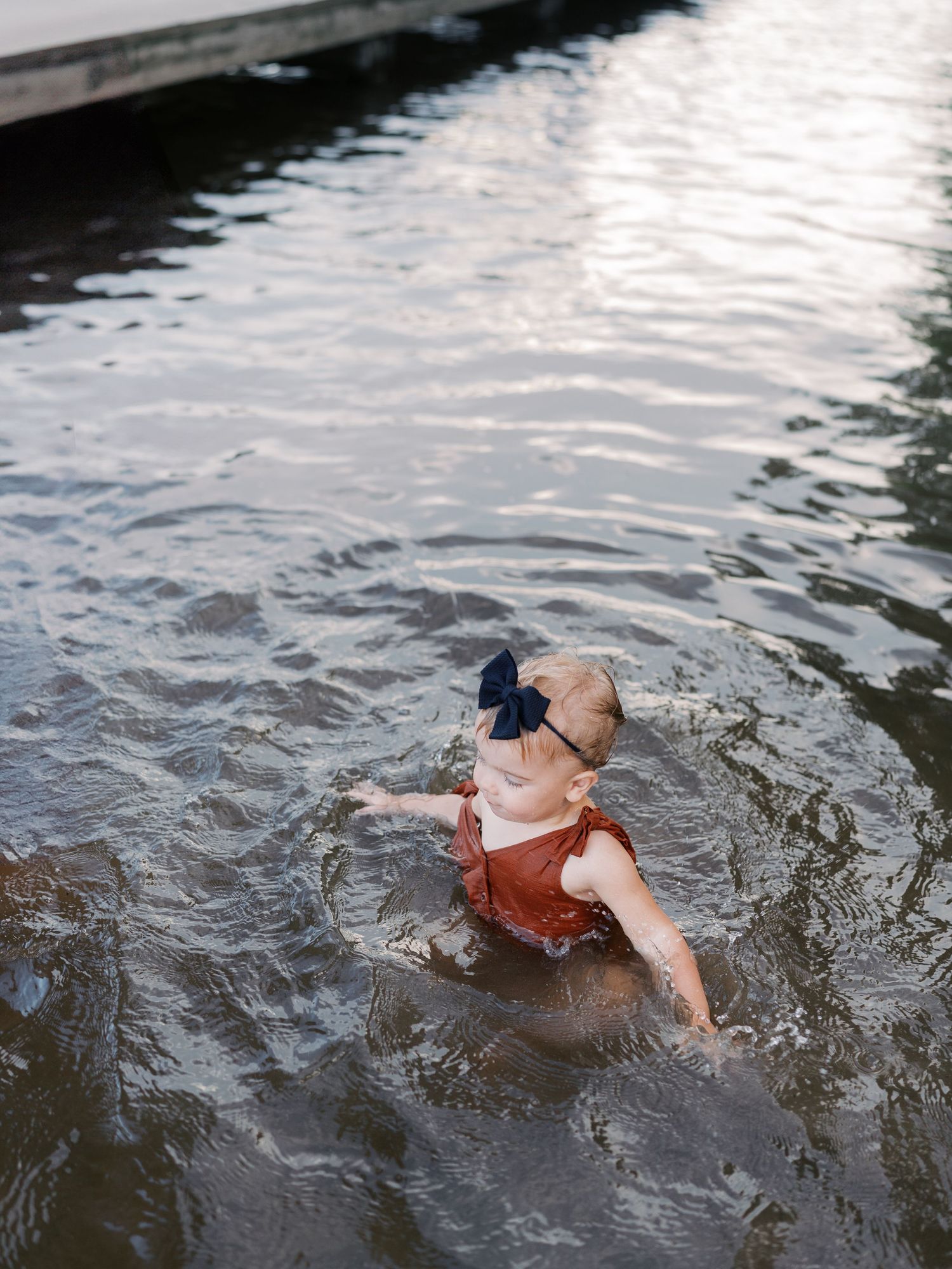 A person wearing a swimsuit splashes into a lake from a wooden dock on a sunny day.
