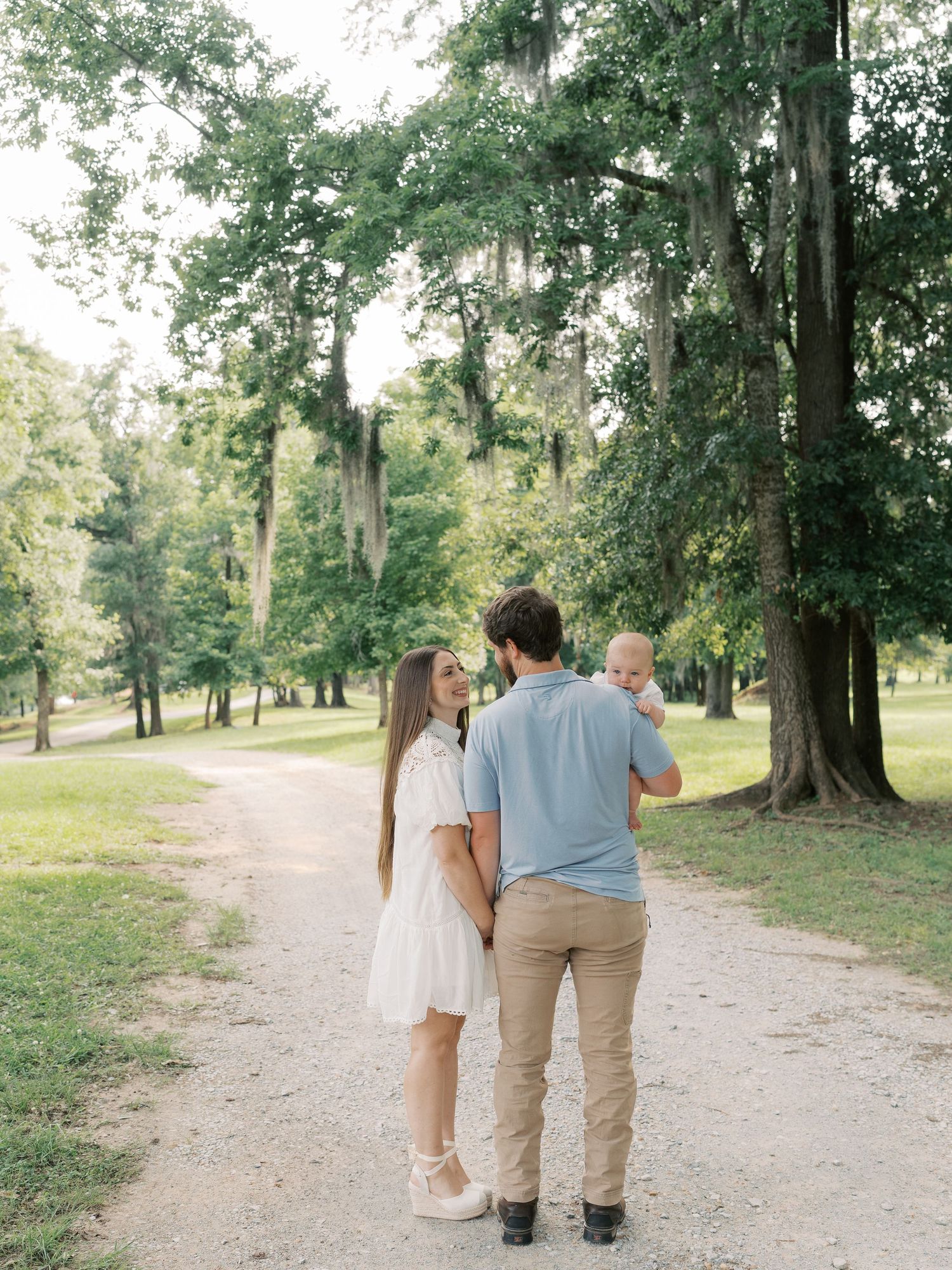 A family walks together down a peaceful dirt trail surrounded by tall trees.