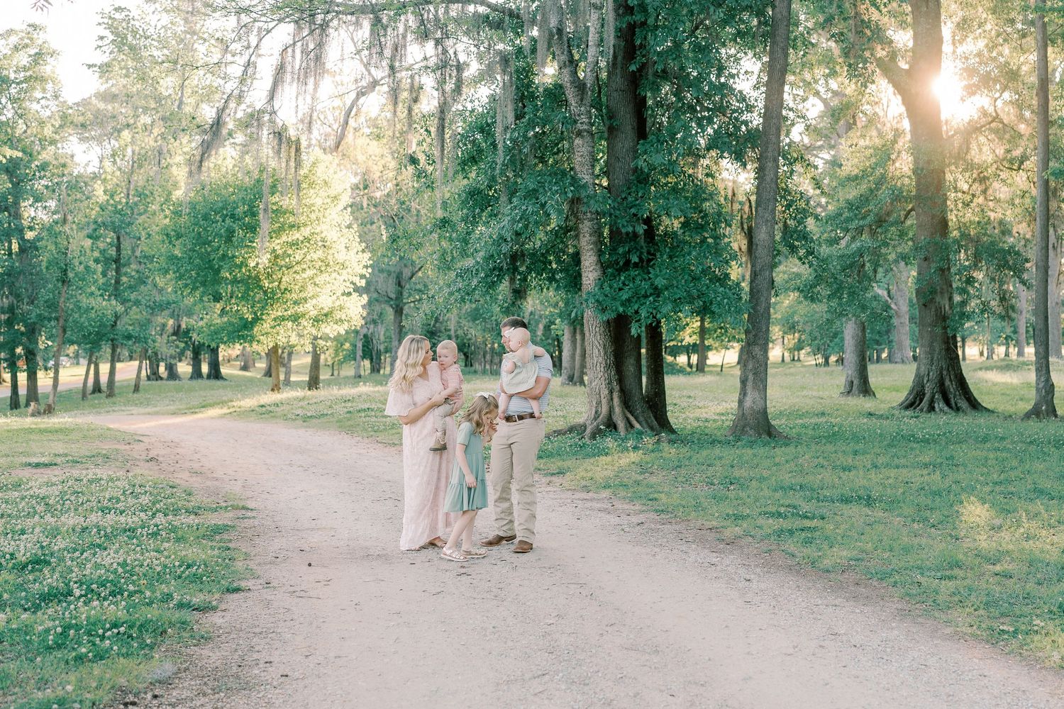 Family photo session on a tree-lined path with warm evening sunlight filtering through.