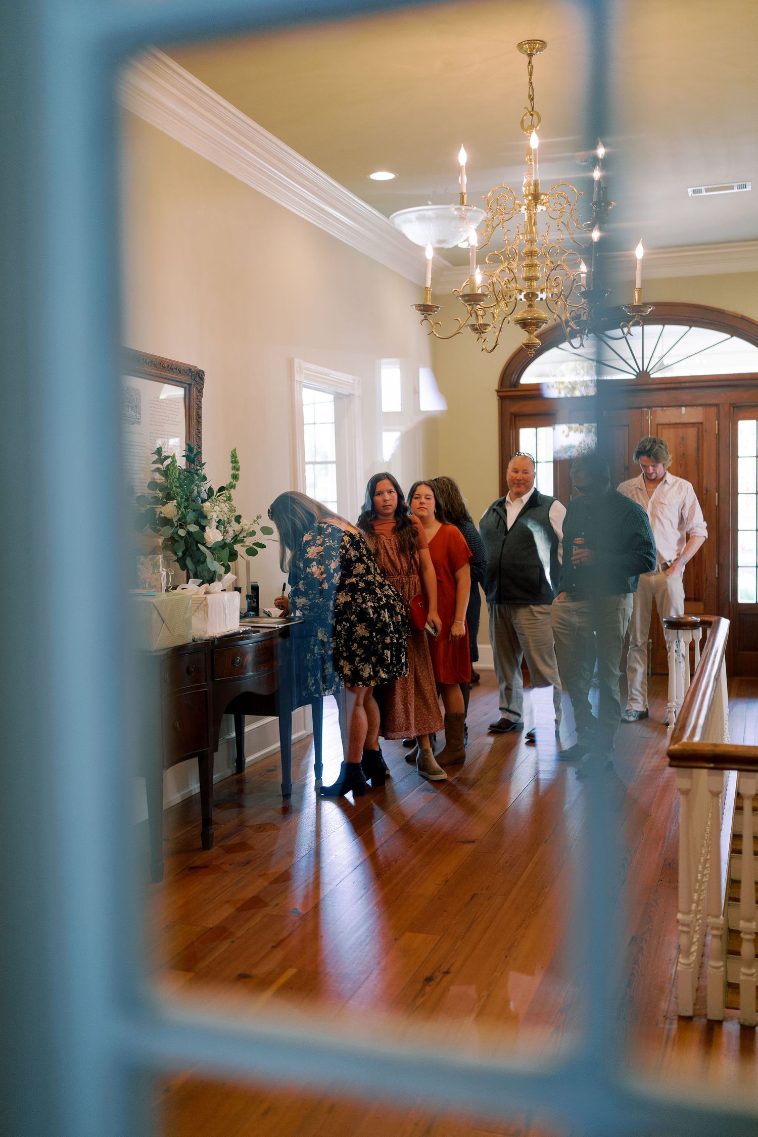 Wedding party gathering in an elegant venue with chandelier and hardwood floors.