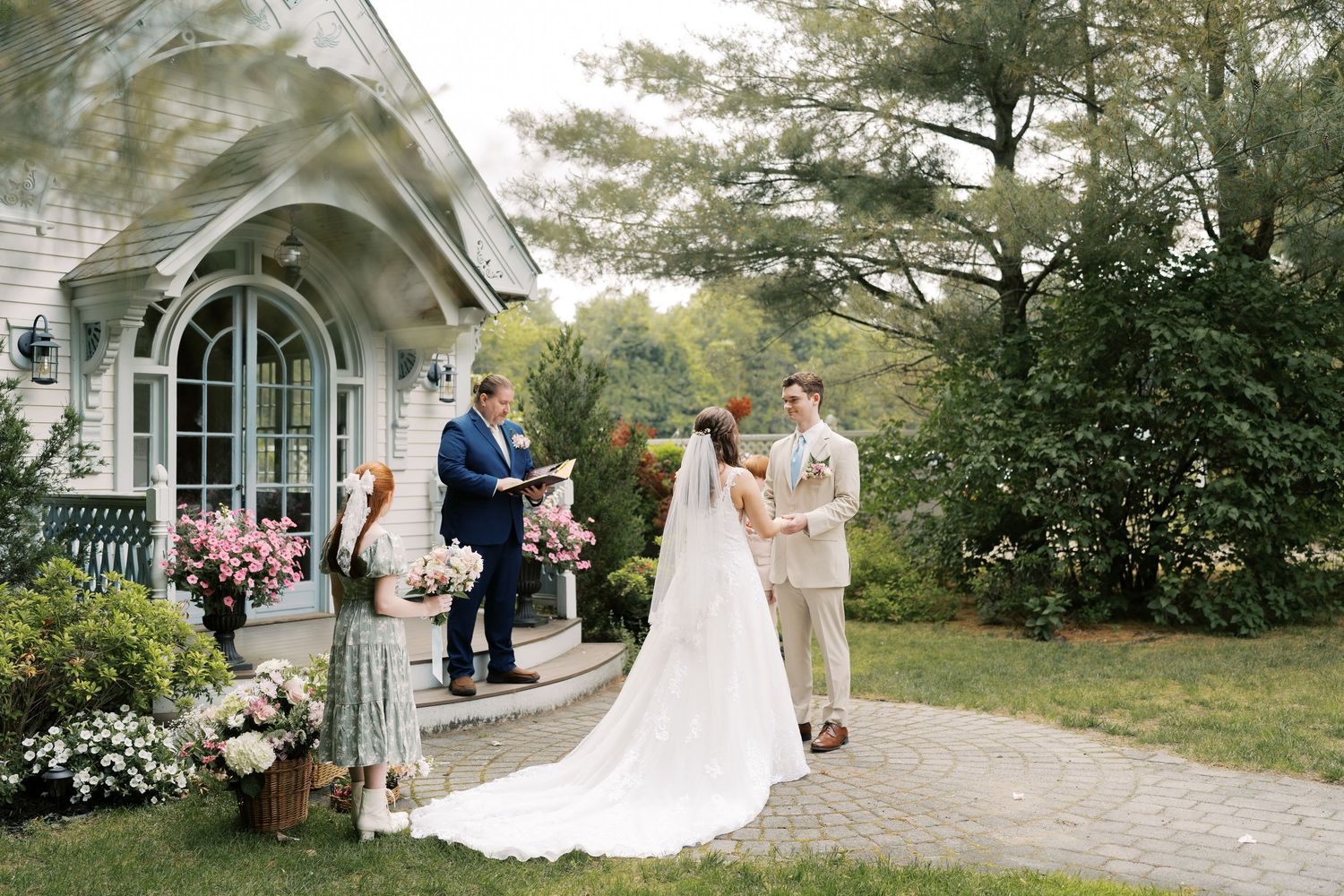 Wedding party gathered outside a charming white chapel with arched windows and lush greenery.
