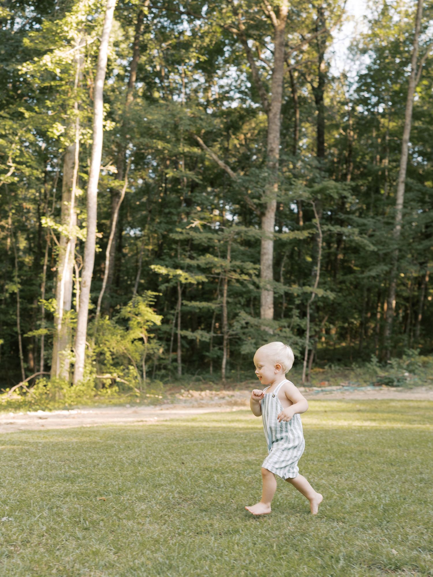 Children run and play in a grassy backyard surrounded by tall trees.
