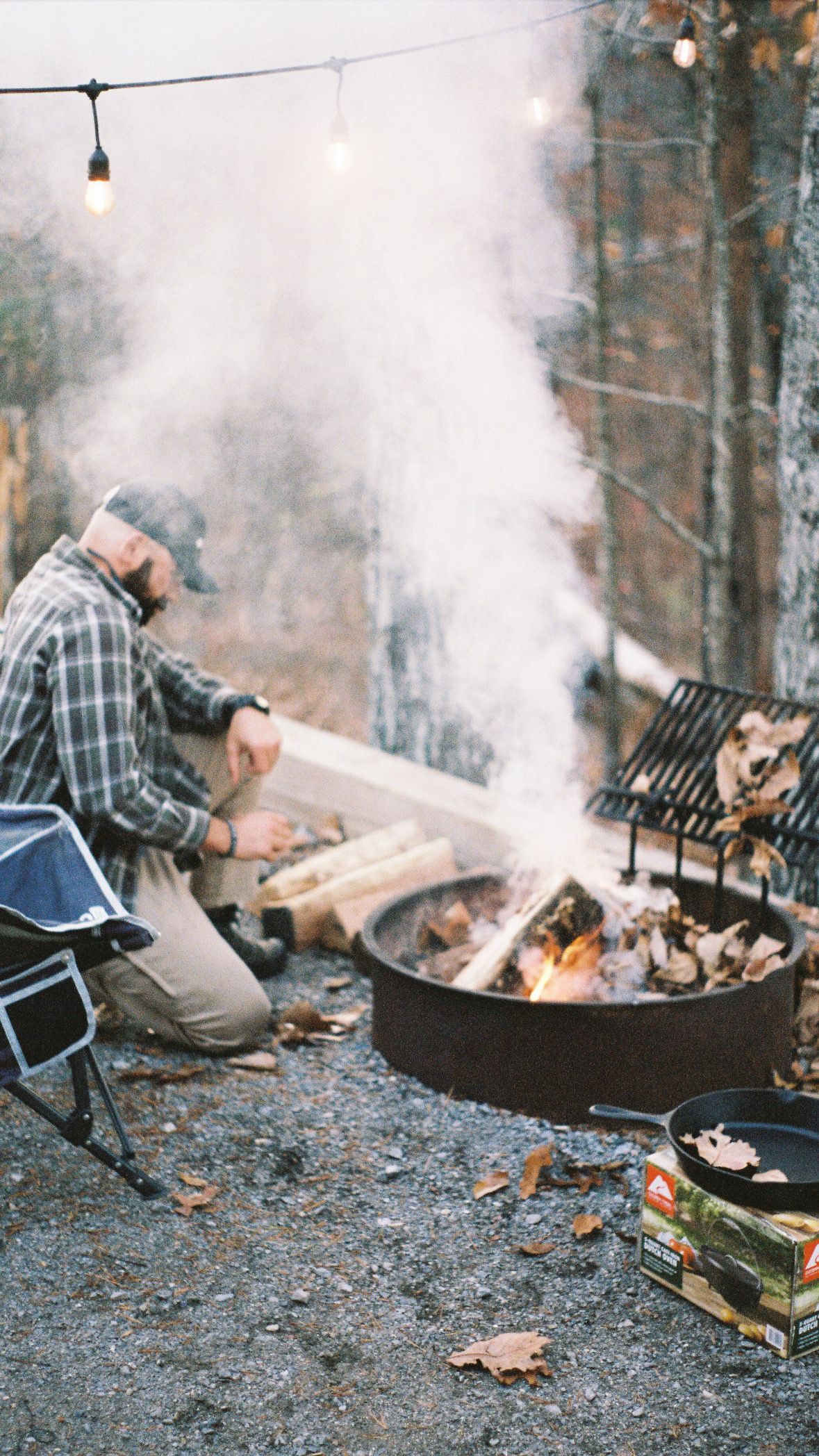 Campfire burning in a metal fire pit with smoke rising on a misty evening.