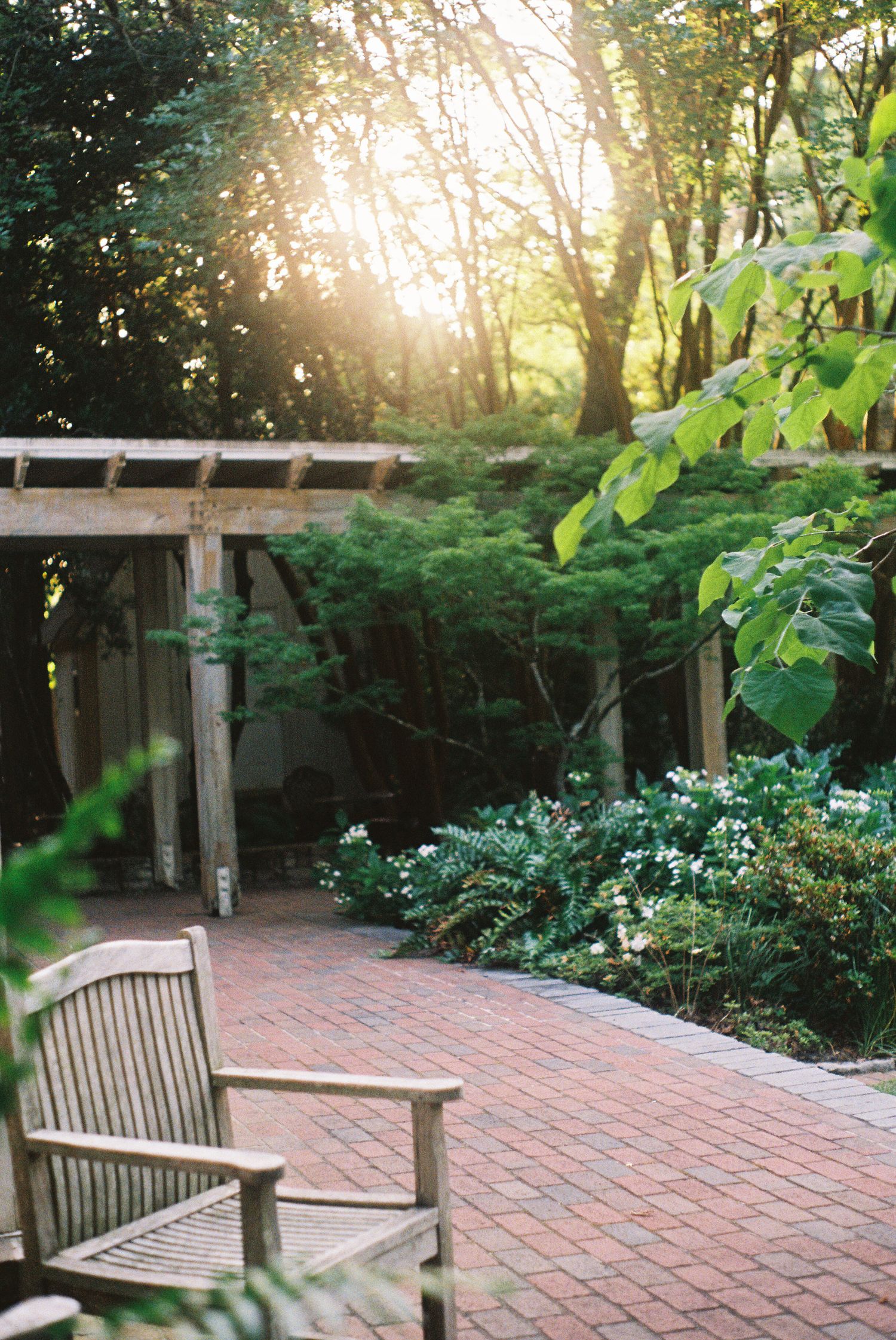 Brick patio with wooden benches surrounded by lush garden landscaping.