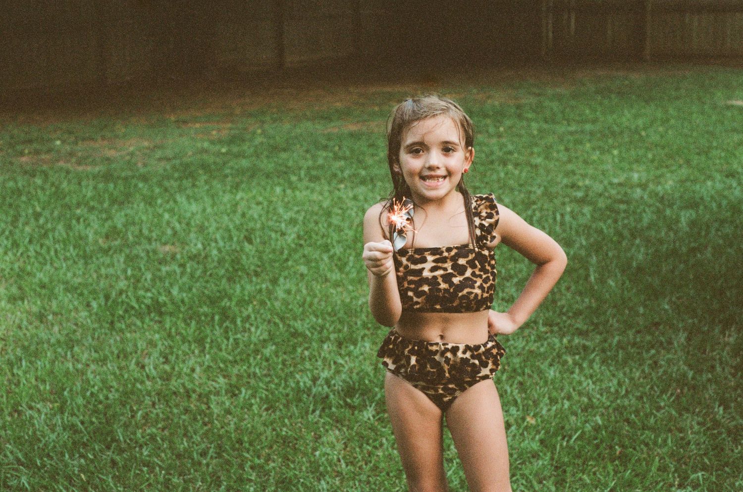 Child in a leopard print swimsuit poses playfully on grass during summer.