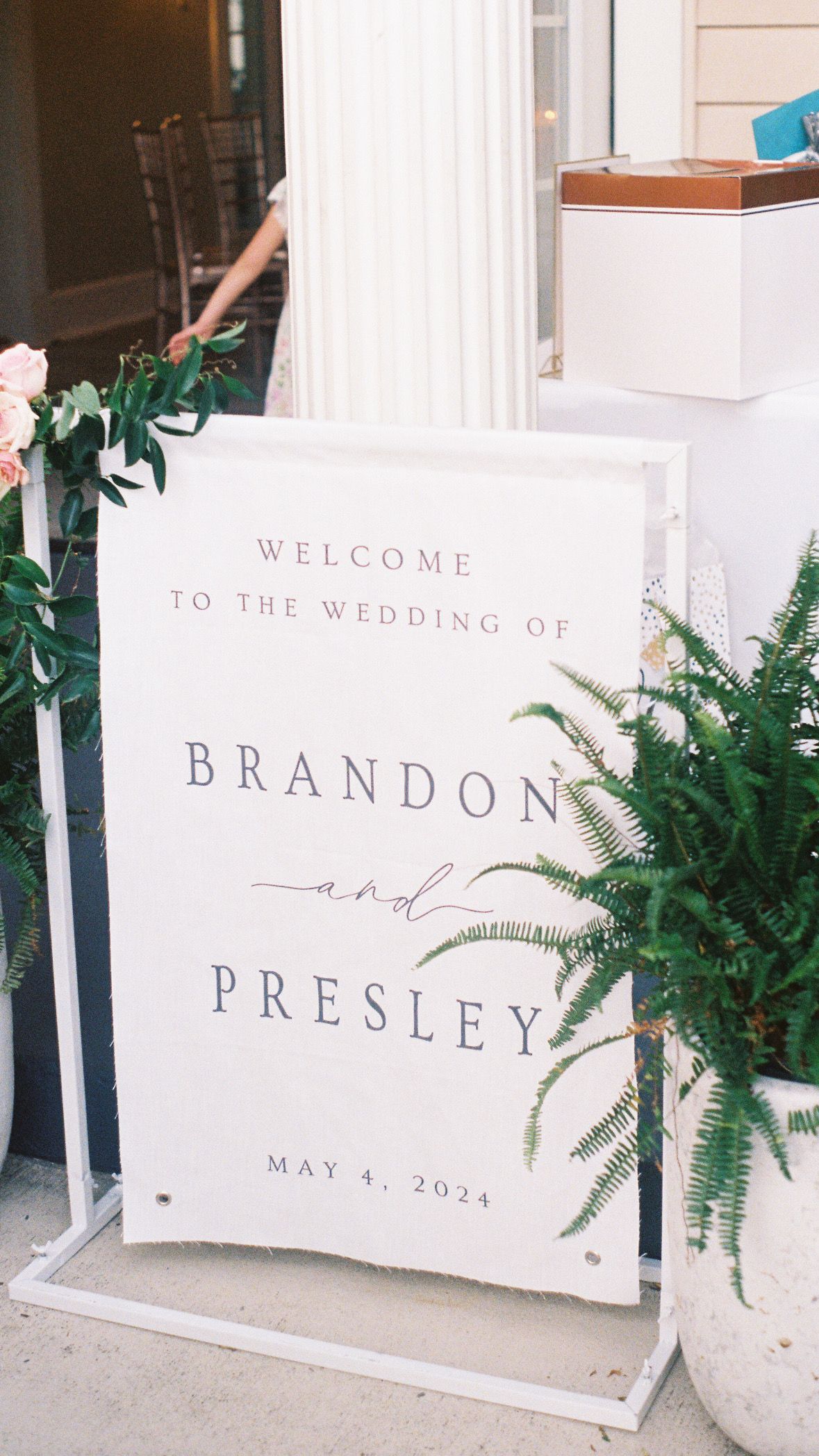 Wedding welcome sign with ferns and elegant typography displaying 'Brandon and Presley'.