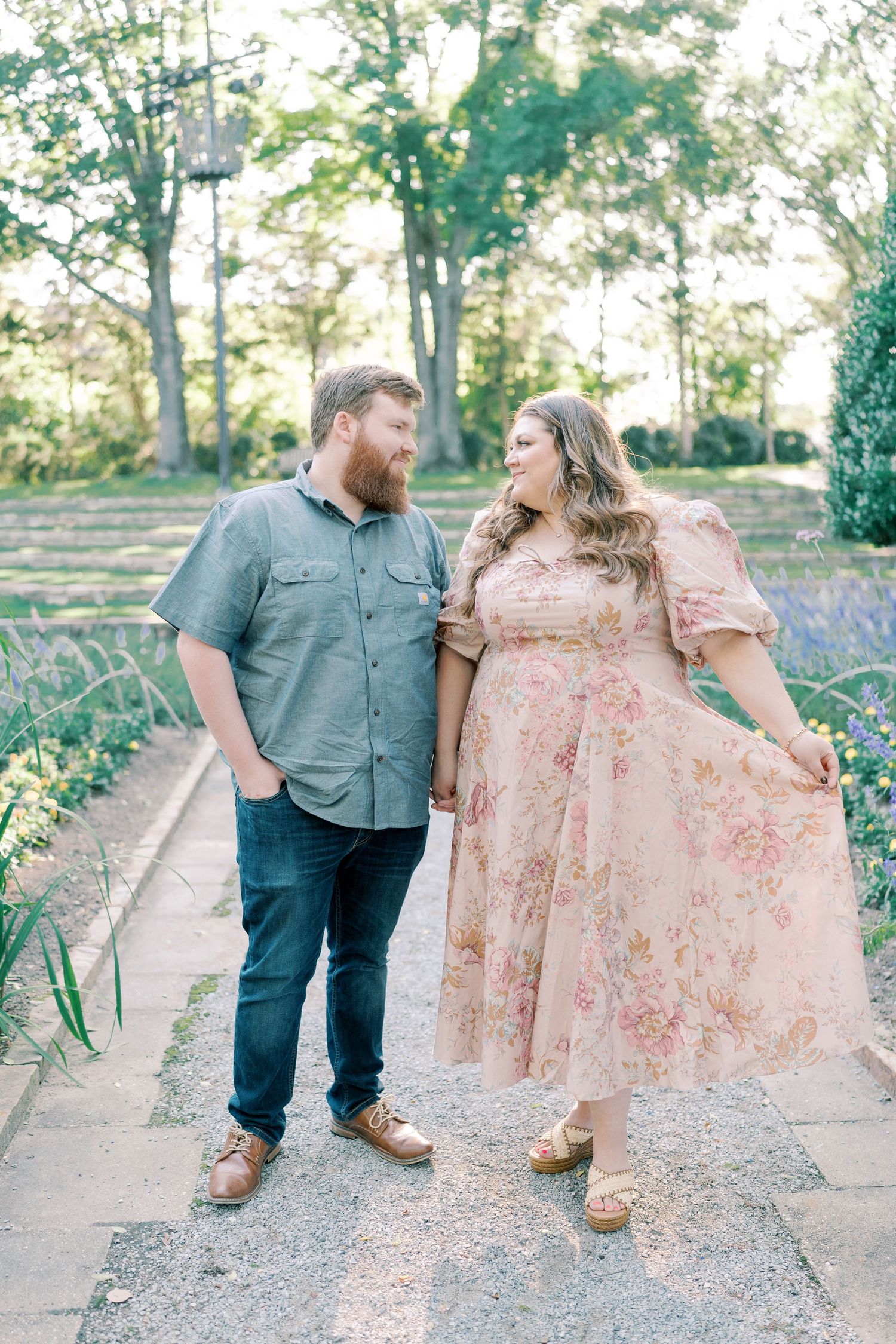 A romantic couple strolling along a garden path wearing pink and grey outfits.