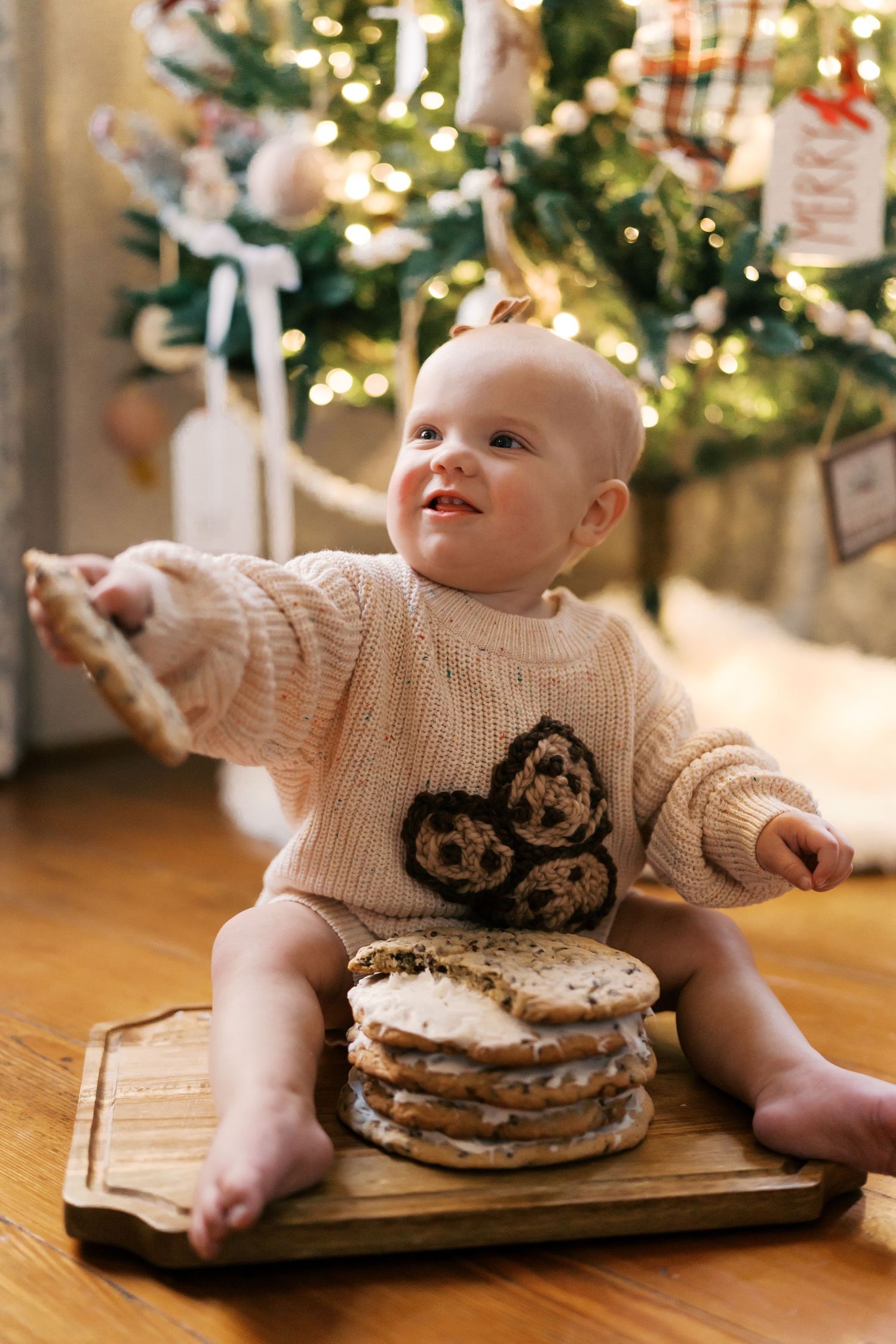 Baby in cream sweater explores pancakes near decorated Christmas tree in sequence of playful photos.
